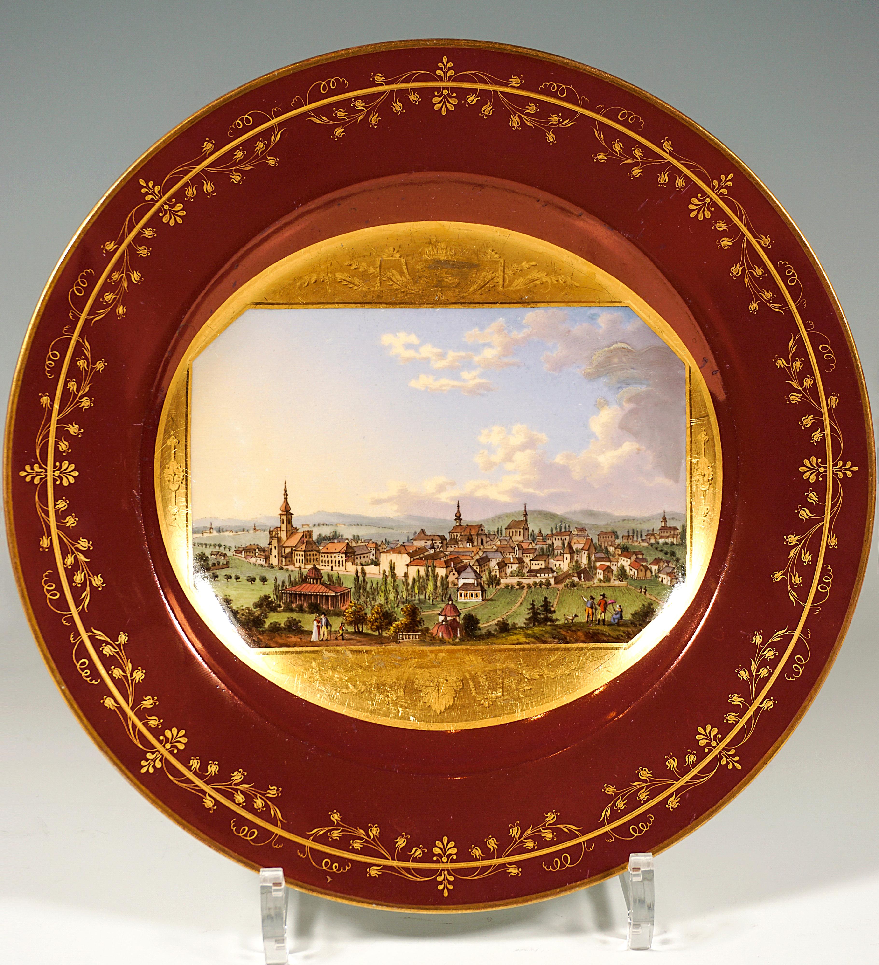 Assiette en porcelaine décorée d'une fine peinture veduta : dans le miroir, panneau pictural octogonal sur fond doré, encadré de festons peints en or mat au-dessus et au-dessous du tableau, représentant la vue de Baden bei Wien depuis le