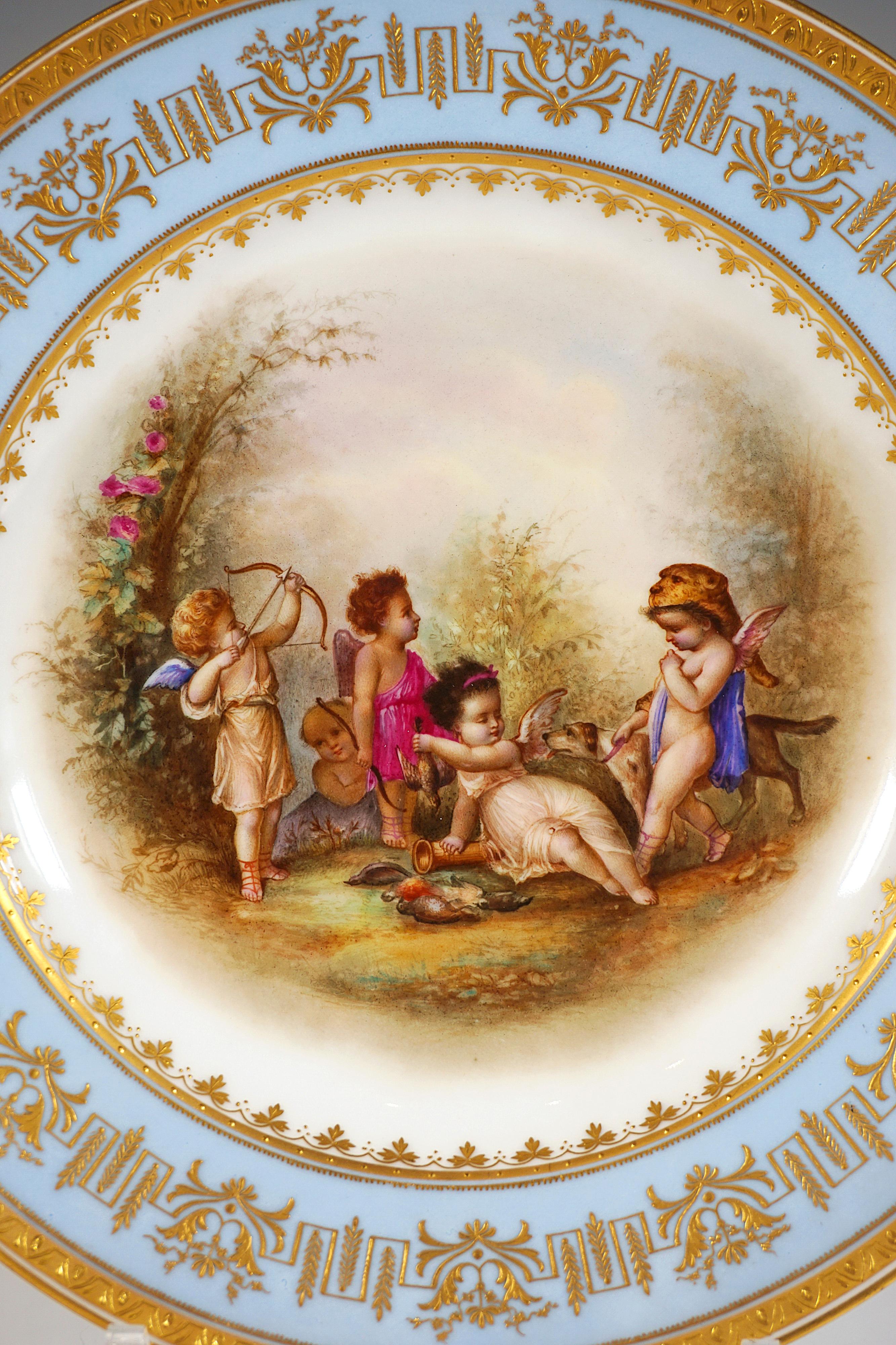 Porcelain picture plate with fine polychrome painted scenery:
In the mirror five winged cupids dressed as hunters with dog in a summer landscape against a white background, framed by golden leaf garland, plate flag in light blue with delicate