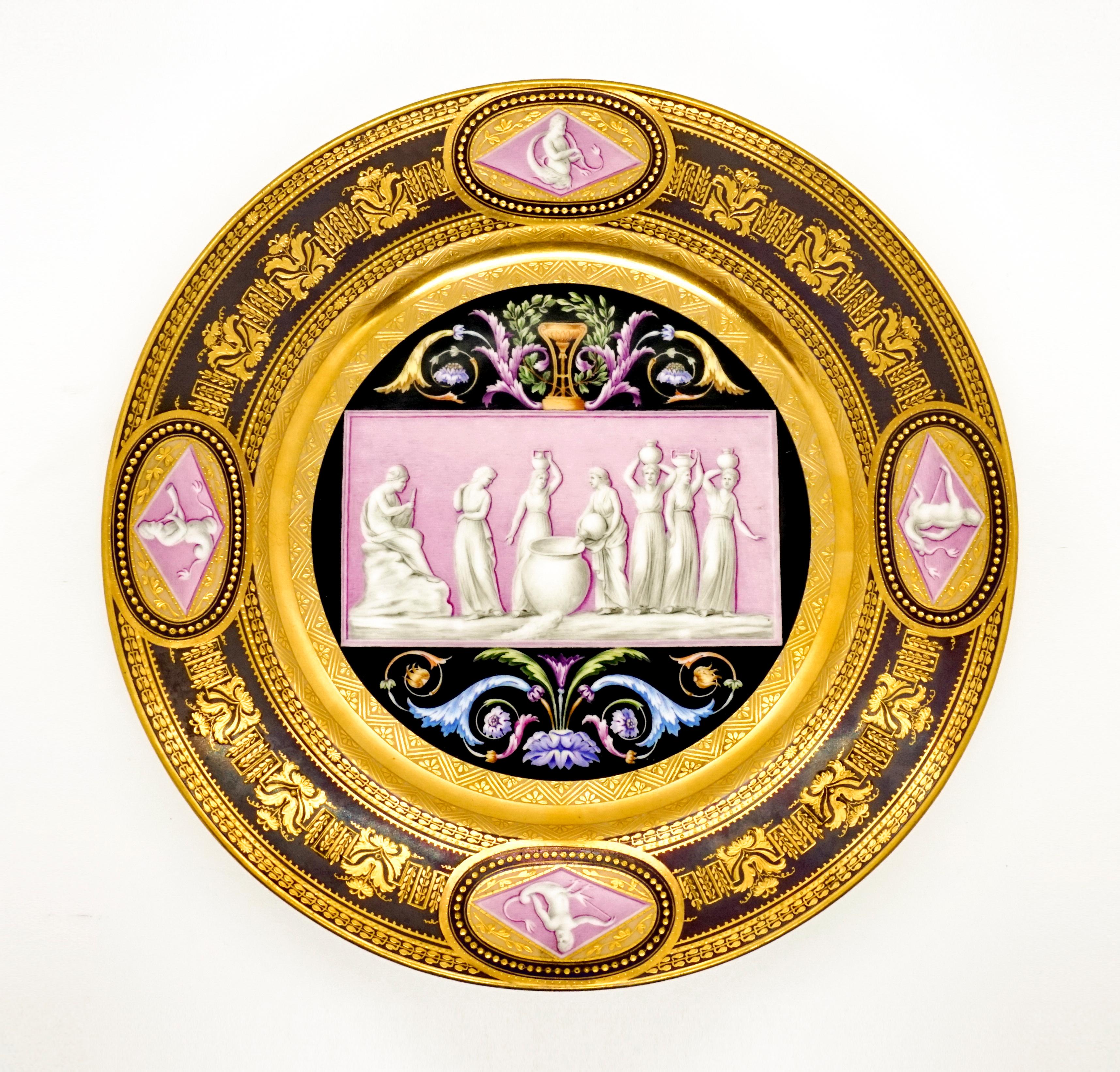 Extraordinarily decorated porcelain plate: in the mirror a pink, transversely rectangular picture panel against a black background, framed by brightly colored leaf and feather tendrils in the segments on the long sides, a cup 
and laurel wreath on