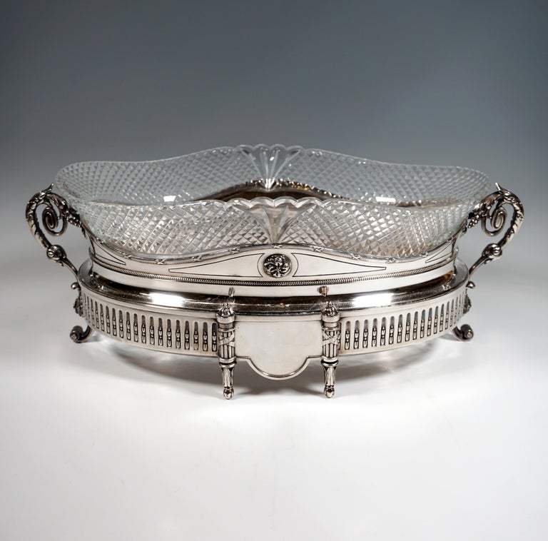 Large silver jardiniere over an oval ground plan, standing on six feet, vessel body with straight walls, lower zone circumferentially provided with fluting with embedded stylized flower buds, front and back center each with a panel, flanked by two