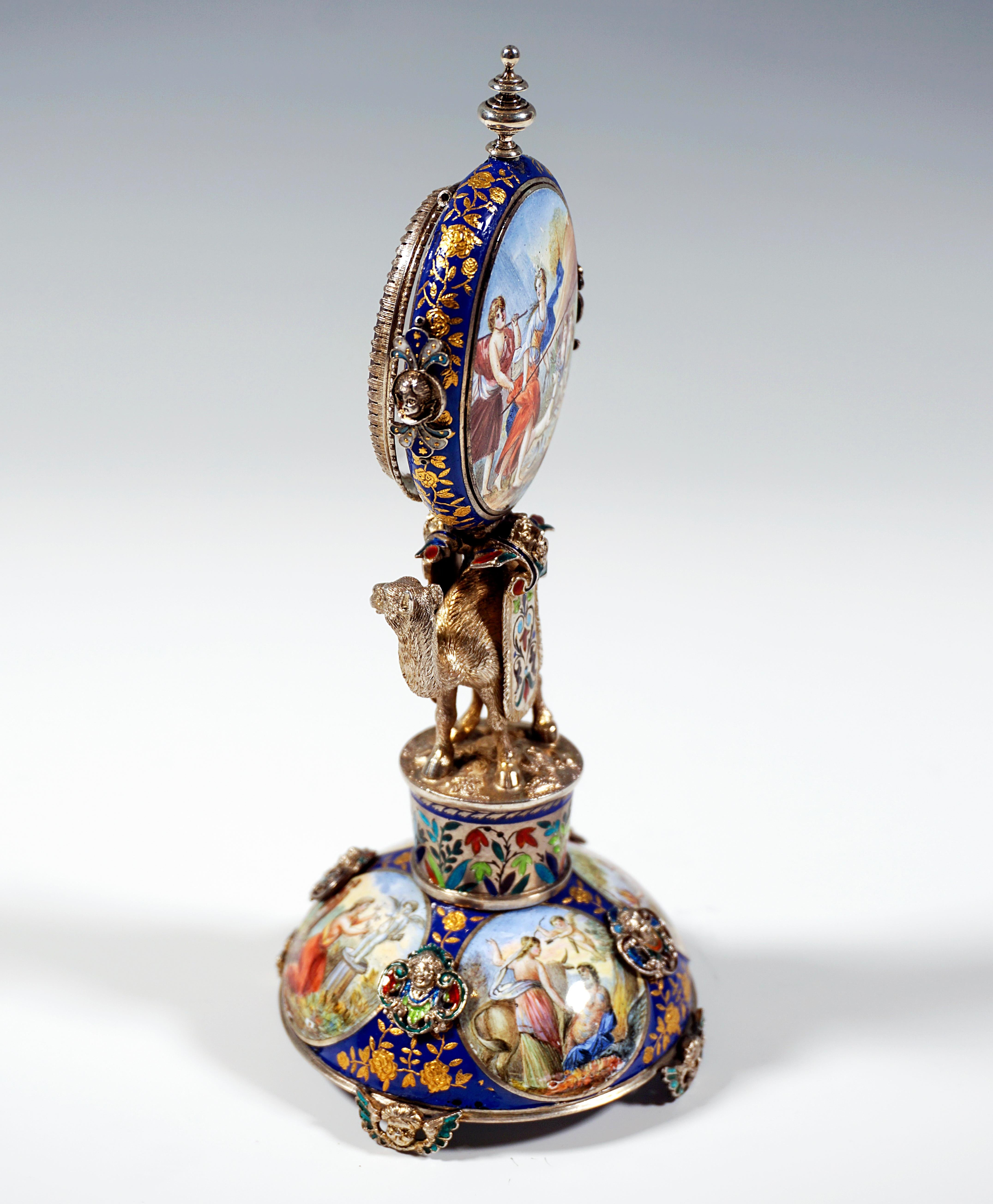 Artfully decorated silver clock by a Viennese master:
Plastic silver camel on a drum carrying the oval watch case, based on a round, curved base with fine enamel painting - four medallions with antique scenes on a dark blue background with flower