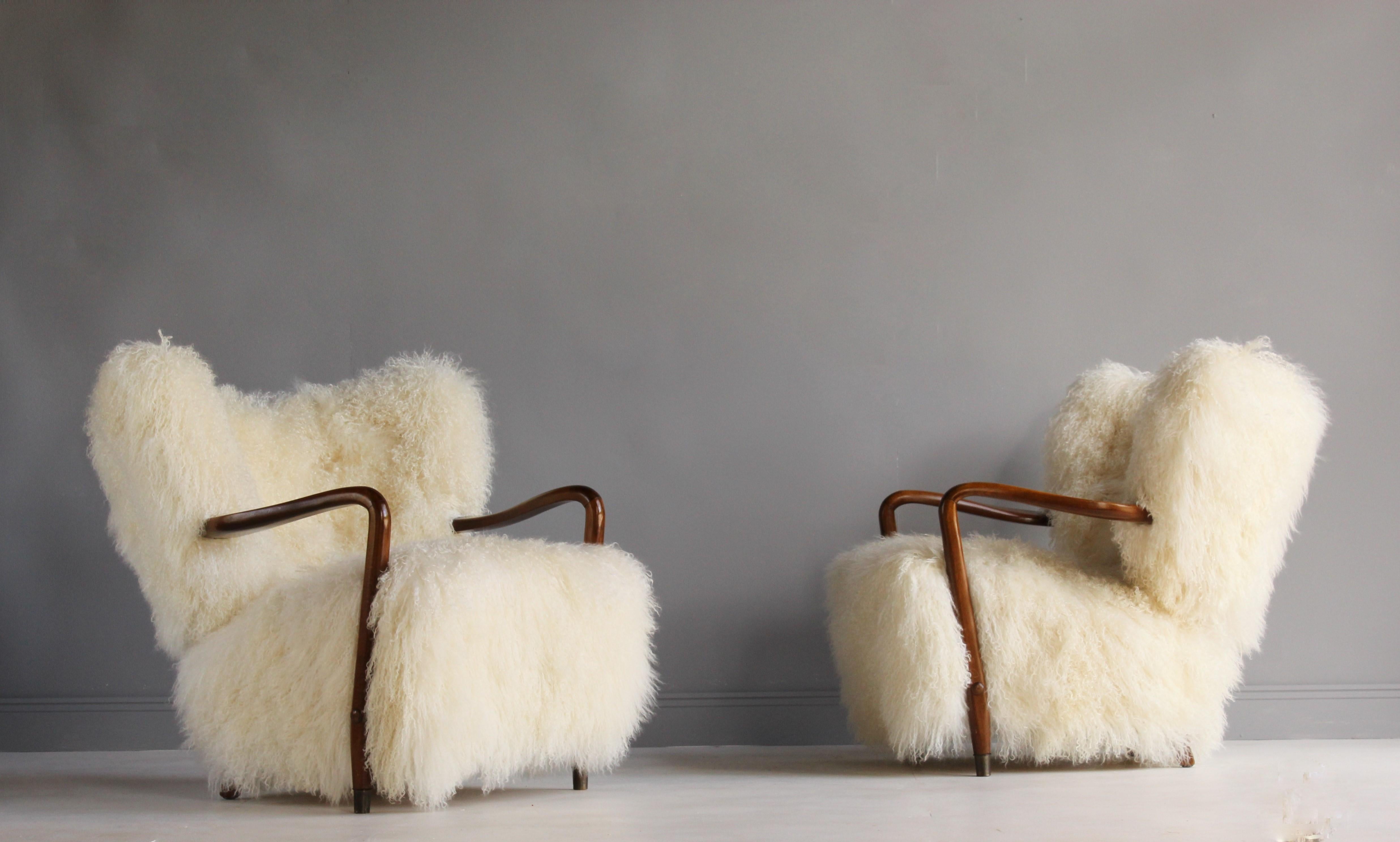 A pair of organic lounge chairs attributed to Viggo Boesen. The softness of organic form is further enhanced by the authentic white lambskin upholstery. The overstuffed form is contrasted by original, dark stained beech arms and legs. Front legs