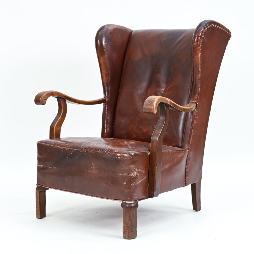 A handsome traditional-style wingback lounge chair, c. 1940's, that marks the turn towards Scandinavian modern design. This armchair features what appears to be the original patinated brick red leather with a tacked trim detail and wooden arms and