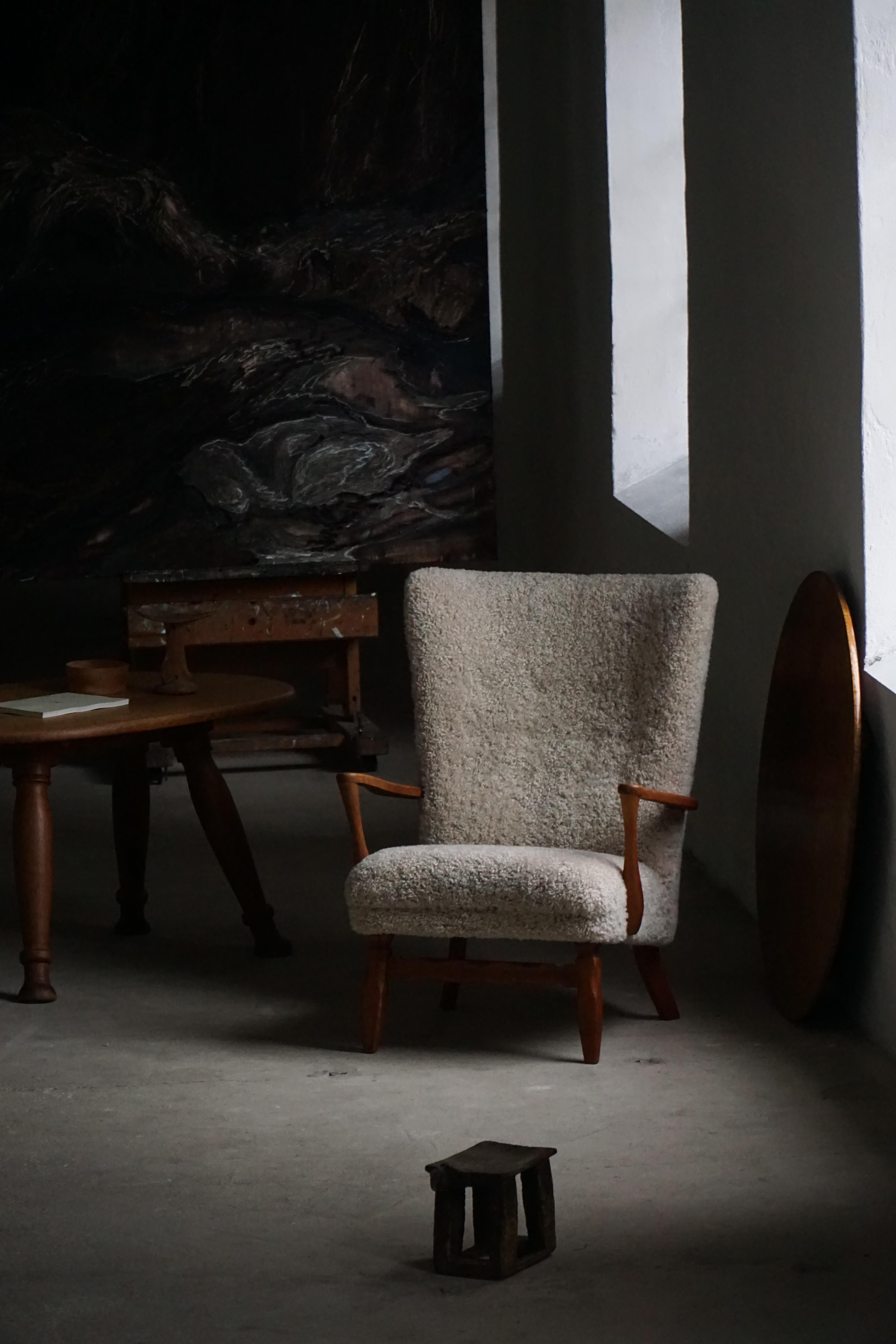 Wir präsentieren einen charmanten Loungesessel mit hoher Rückenlehne aus den 1950er Jahren, gefertigt aus massiver Eiche und sorgfältig neu gepolstert mit einem hochwertigen Lammfell in 