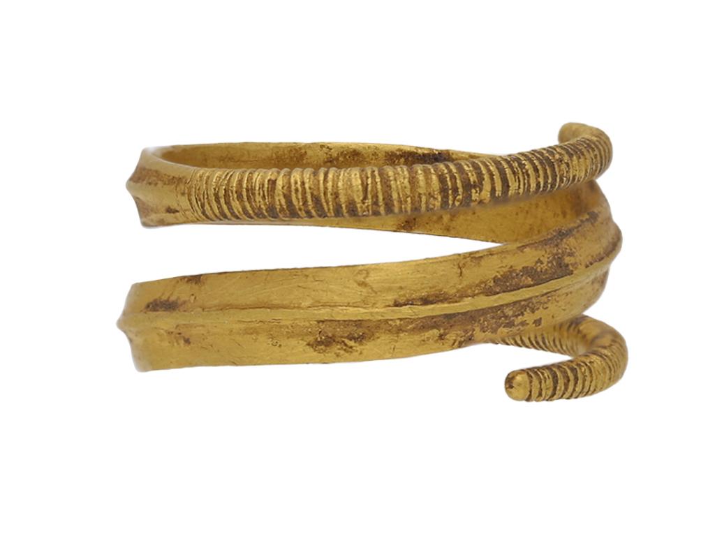 Viking gold coiled ring. A yellow gold sinuous spiraling ring, the subtly hammered band ornamented to the centre with a raised ridge which tapers to rounded incised terminals, all smoothly curving around the finger. Tested yellow gold, approximately