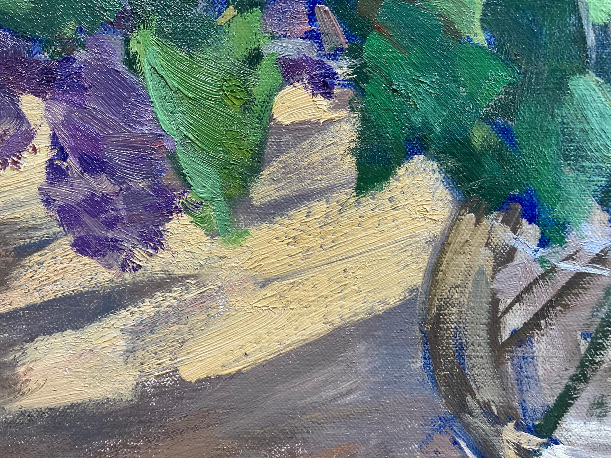 Una tradizionale natura morta di lillà in primo piano si incontra con una vista impressionistica del paesaggio e del cielo fuori dalla finestra. All'interno di una stanza dai toni neutri, un tavolo rotondo di legno sostiene una brocca di vetro ricca