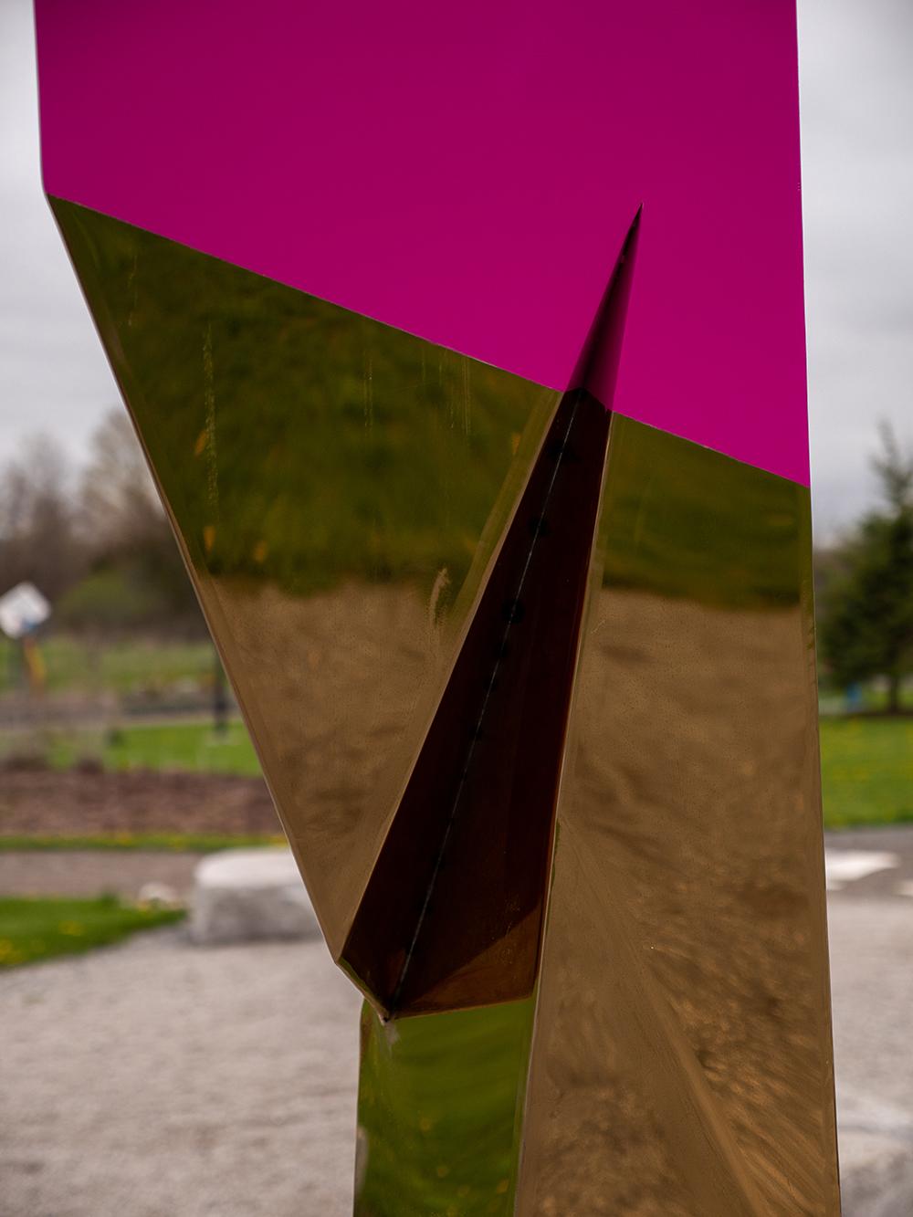 Cette sculpture extérieure de Viktor Mitic, hautement réfléchissante et plaquée or, est visible de loin en plein soleil. Créée à partir de rendus 3D d'angles aigus, la forme prend une apparence ailée. La colonne des résumés est unique et non éditée.