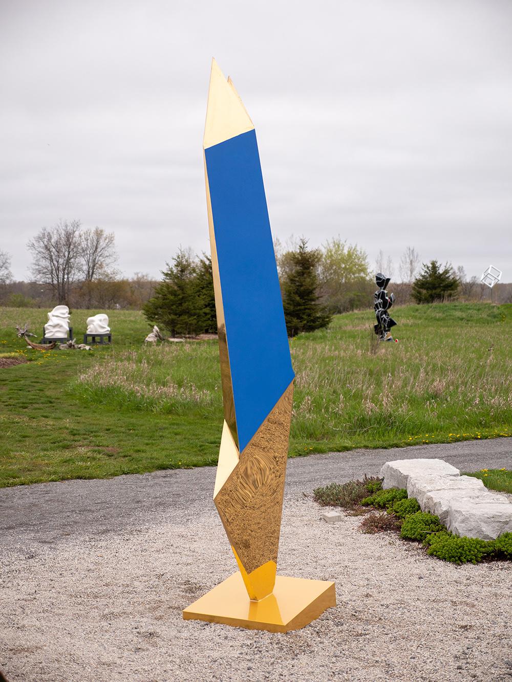 This highly reflective, gold electro-plated outdoor sculpture by Viktor Mitic is visible at a distance in full sun. Created using 3D renderings of acute angles, the form takes on a winged appearance. The abstract column is unique, not editioned. It