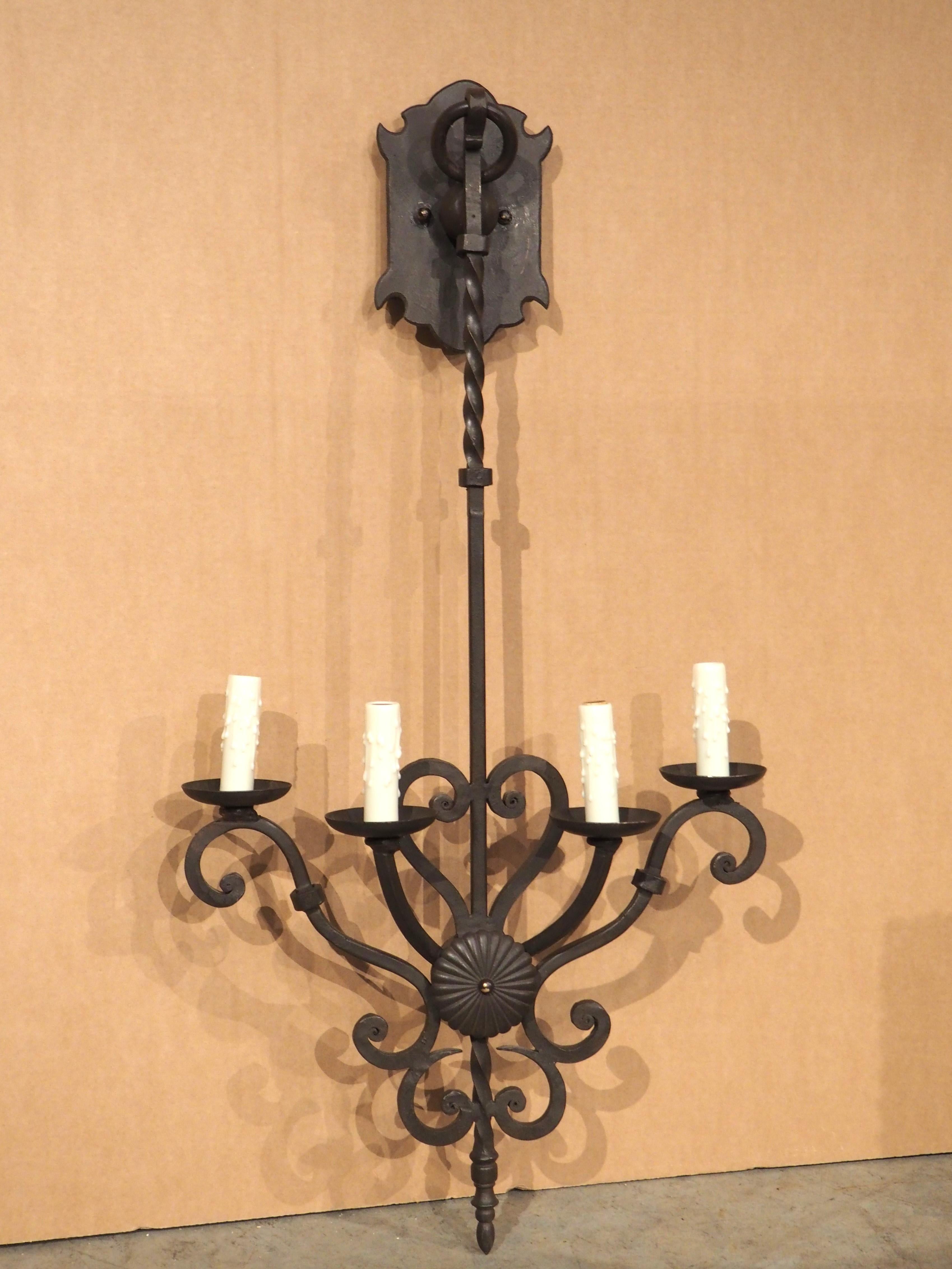 This four-arm wall sconce features a long twisted column that allows the lights to hang beneath the shaped backplate with a ring finial. The shaft is affixed to the backplate by a large roundel, just above a turned section. As the column extends
