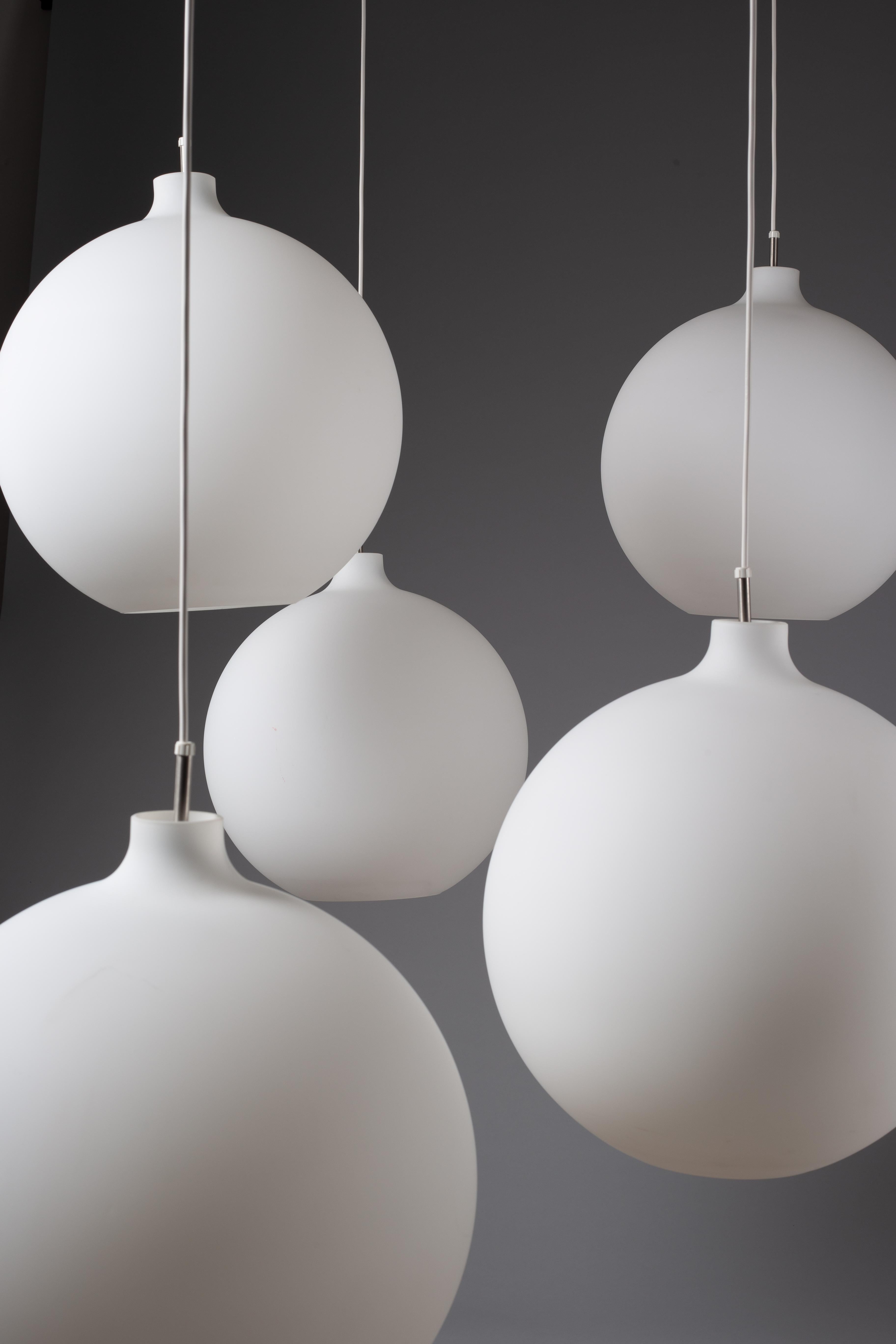 Aggiungi un tocco di eleganza senza tempo al tuo spazio con le lampade a sospensione Vilhelm Wohlert Satellite, realizzate in esclusiva per Louis Poulsen. Questo raffinato set di 5 apparecchi in vetro opalino illumina meravigliosamente gli interni,