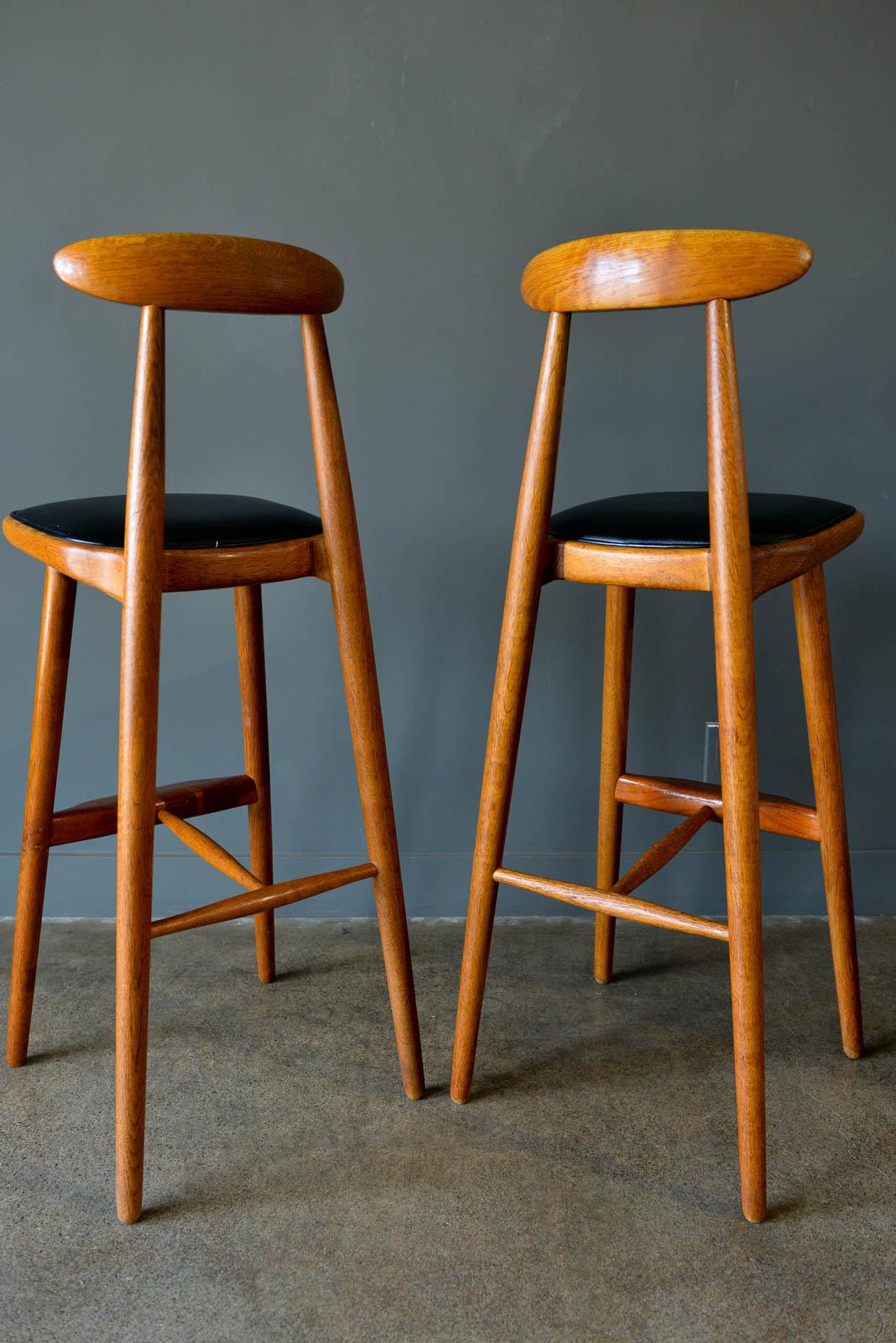 Vilhem Wohlert pair of teak barstools, circa 1960. Matching pair with sculpted oak frame and old growth teak footrest with original black vinyl seats in good condition with only slight wear. Solid wood, no veneer. Totally original and unrestored,