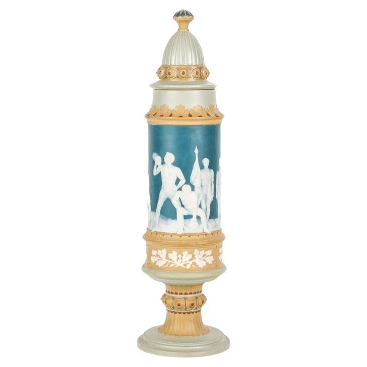 A pokal or large standing cup with Classical gymnastic and athletic scenes around the body. Circa 1880 - 1932; possible from Jean-Baptiste Stahl. The tall lidded vessel depicts male athletics engaged in wrestling, weight lifting, and exercise bar.