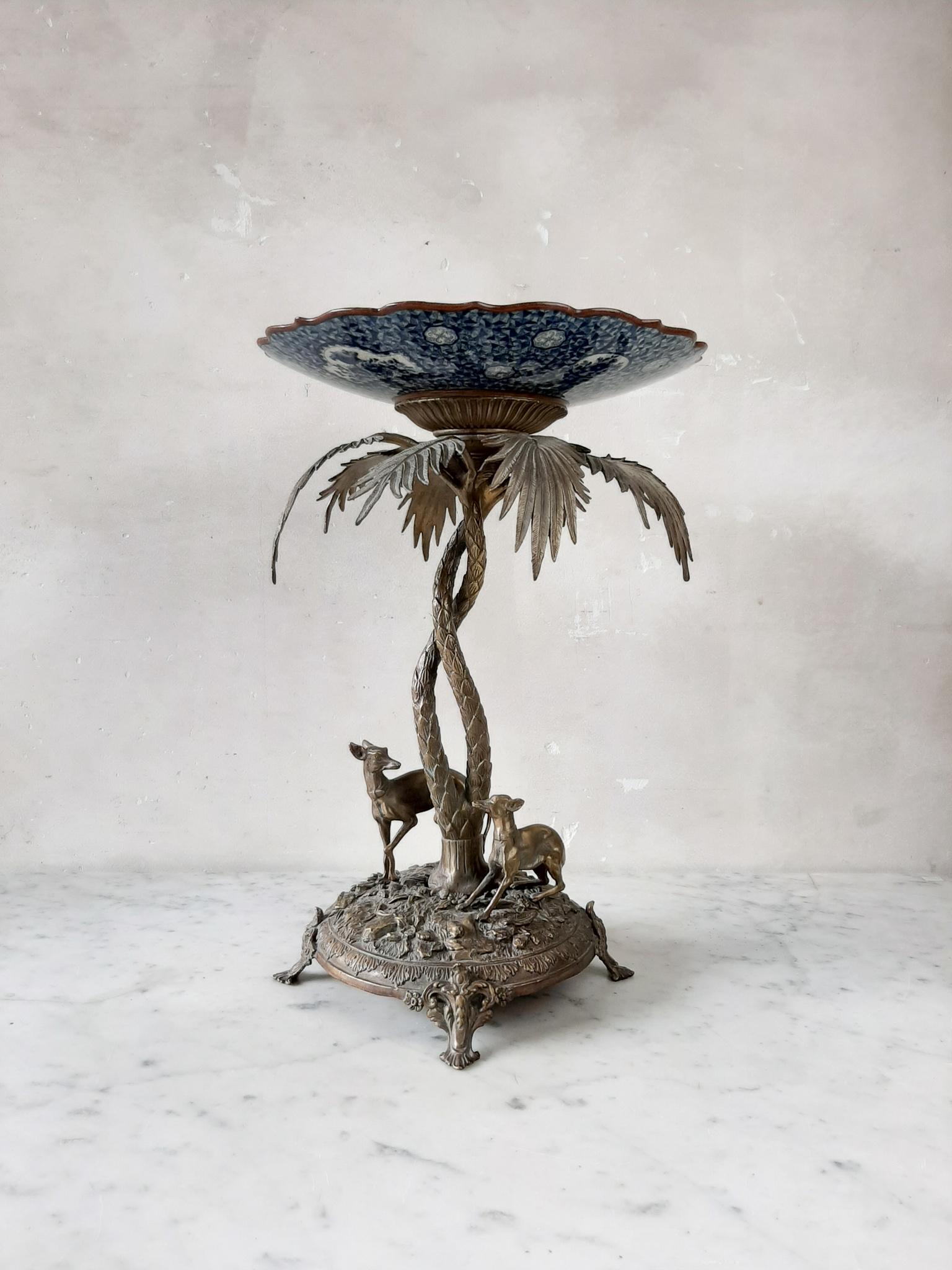 A beautiful detailed centerpiece, two whippets under a palm tree. A Villeroy & Boch plate in blue and white ceramic, above a shaped bronze base, with two entwined palms sheltering two dogs or greyhounds, modeled after Pierre-Jules Menne's Two