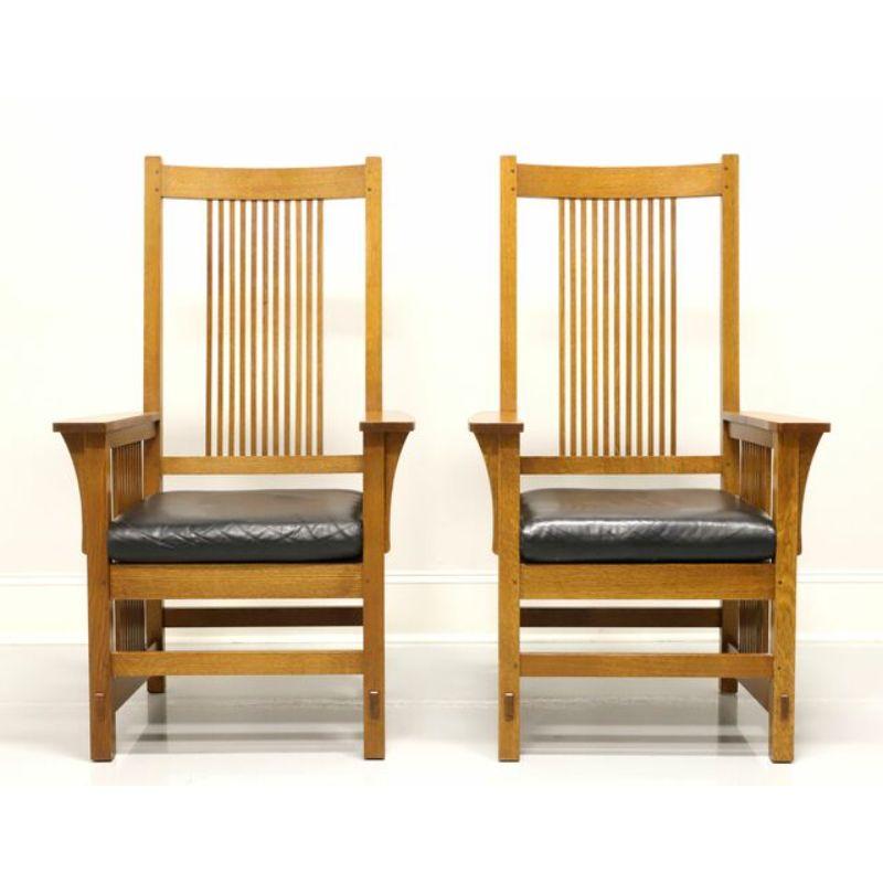 A pair of dining armchairs in the Mission style by Stickley. Oak with tall open slat backs, flat arms, black leather seat support with black leather upholstered cushion and straight legs with side open slat base joined by slat stretchers. Made in