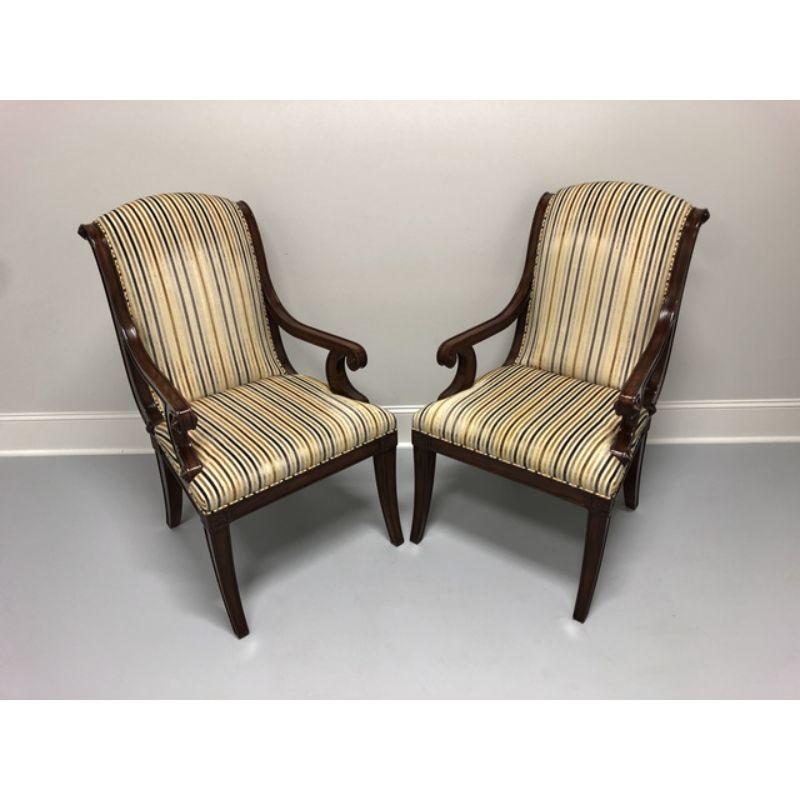 A pair of upholstered armchairs by Theodore Alexander, their Gabrielle. Mahogany frame, over scroll padded back and seat between open scroll arms and above floral capital carved and paneled sabre legs. Velvet-like stripe upholstery fabric. Inspired