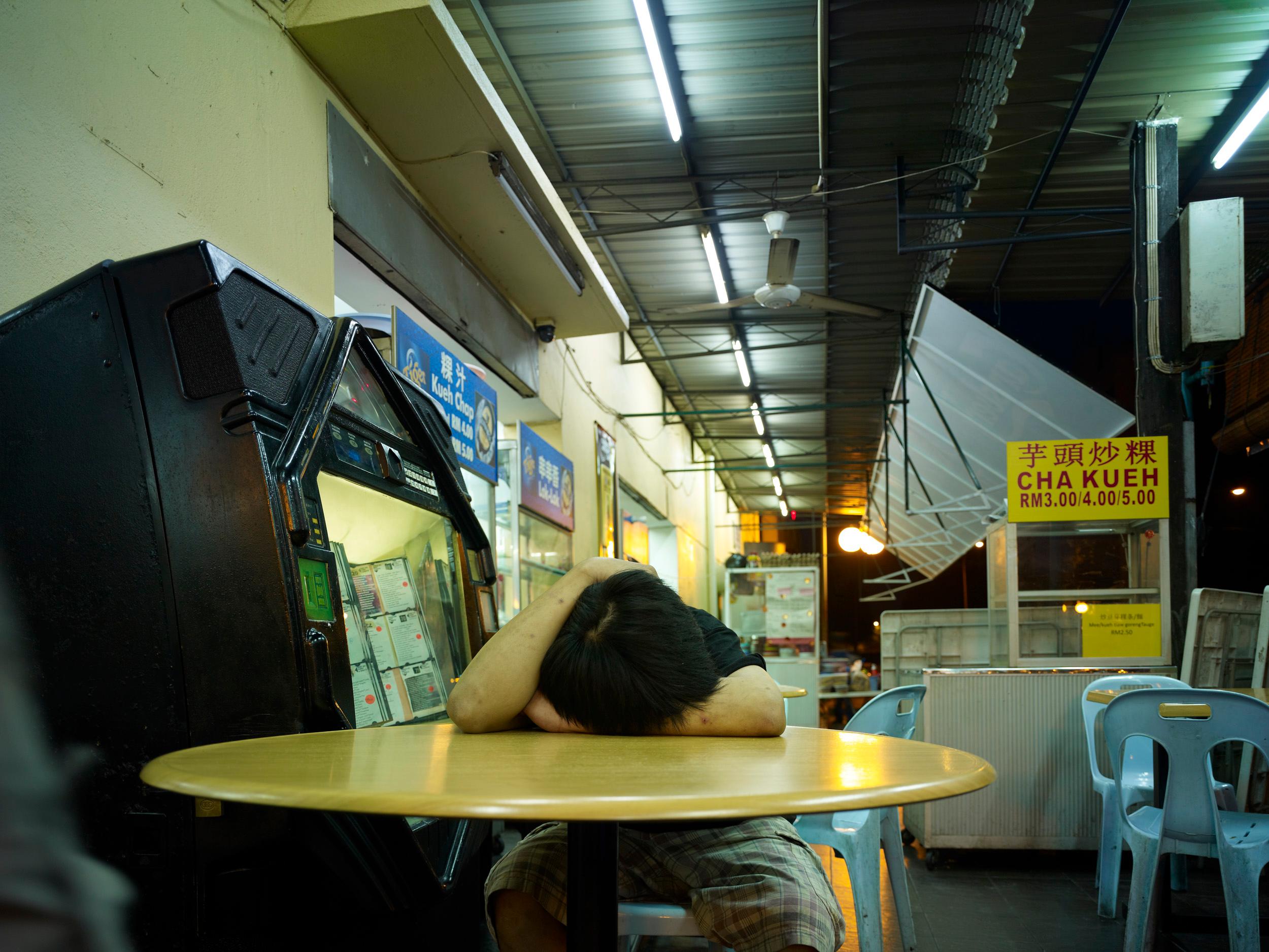 Borneo 4: photograph of sleeping man at yellow cafe table, Southeast Asia