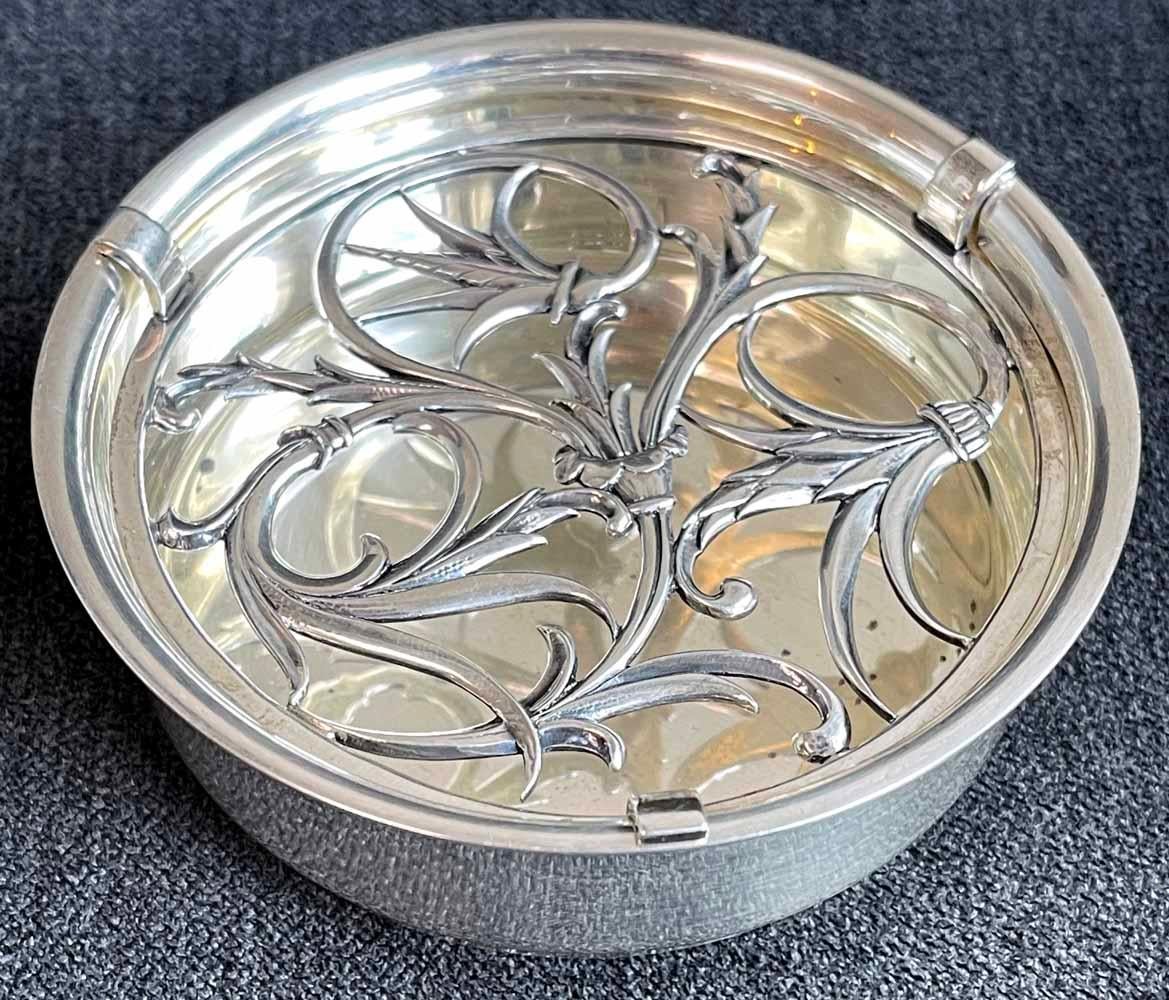 Uno dei più eleganti e sofisticati esempi di artigianato Art Déco che abbiamo mai offerto, questo piatto con coperchio forato (originariamente serviva come posacenere) presenta un motivo a viticci e viticci con dettagli raffinati e bellissimi.  Il