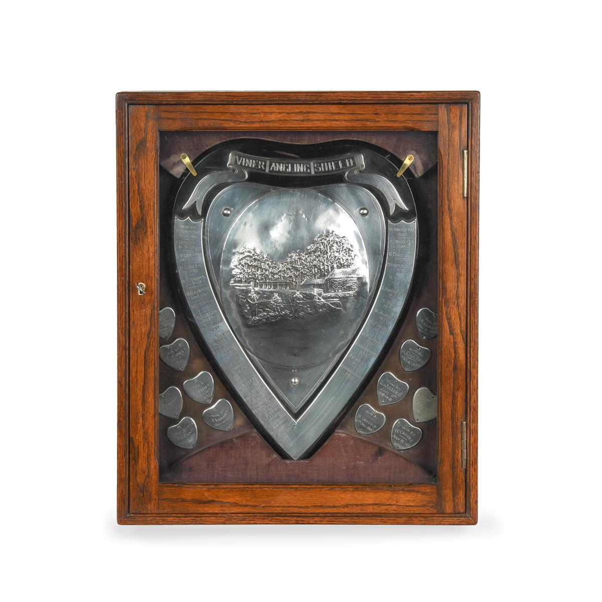 Die Viner Angling Shield Präsentation Angeln Trophäe mit original Fitted Oak Wall Display Cabinet, die herzförmige zentrale Plakette mit geprägter Szene einer Gruppe von Herren Angeln, ein Gebäude und Wald im Hintergrund. An den Seiten der