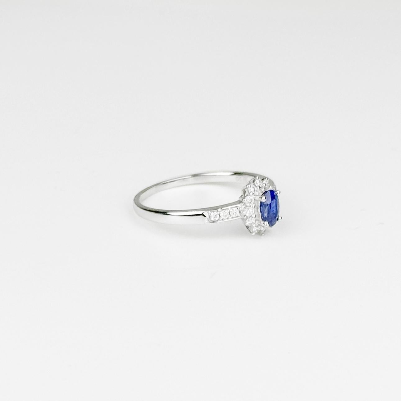 This refined ring is set in 18 karat white gold, featuring a delicate and captivating design. At the center, a 0.36 carat Sri Lanka Sapphire radiates a rich blue hue, known for its vibrant and alluring color. The oval sapphire is framed by a halo of