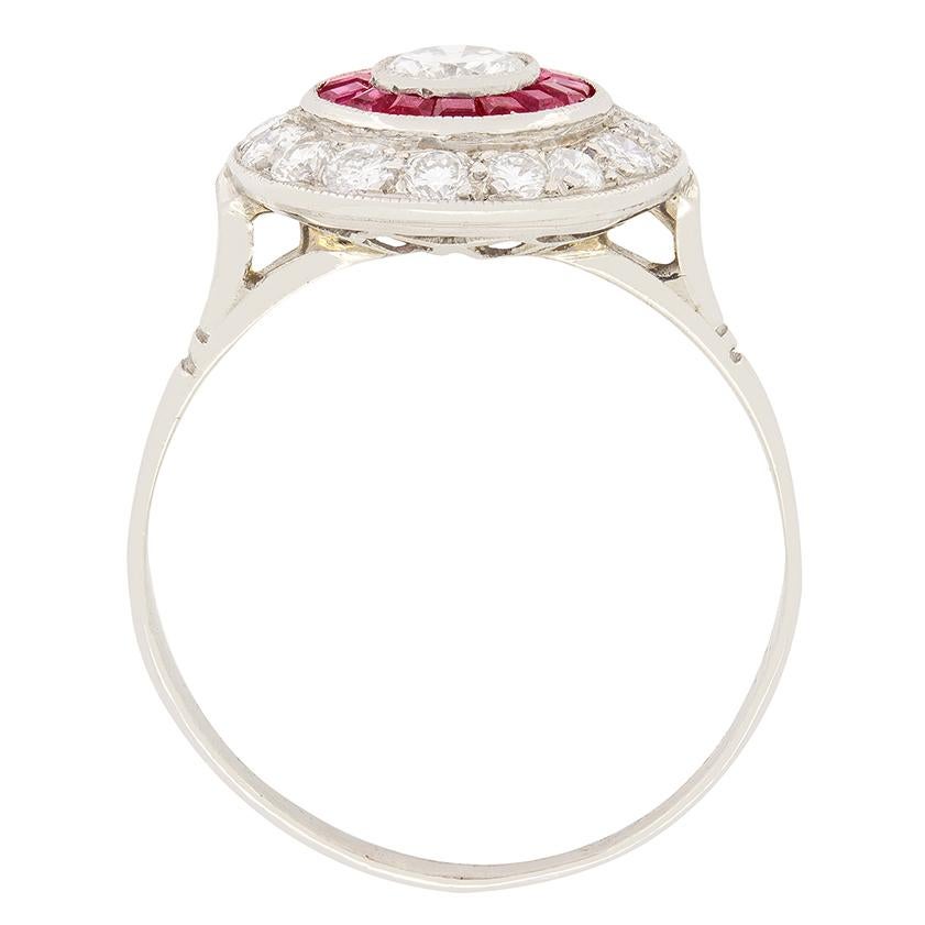 This unique diamond and ruby ring was crafted in the 1950s. At the centre a 0.40 carat round brilliant diamond sits. The rub over set diamond is F colour and Si1 in clarity. Surrounding this centre stone sits a ring of vivid baguette cut rubies. The