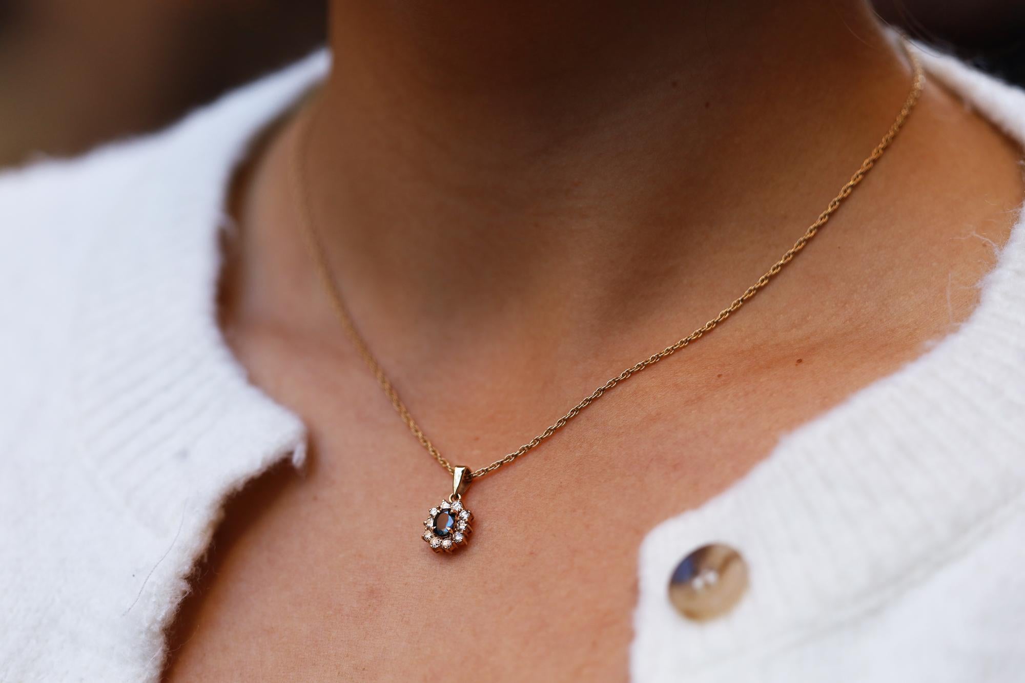 Vintage and affordable, this estate necklace is a perfect everyday pendant. An ever-popular halo design centered with a midnight blue oval sapphire weighing 0.48 carats, encircled with 10 sparkling round brilliant diamonds. Made with 14 karat yellow