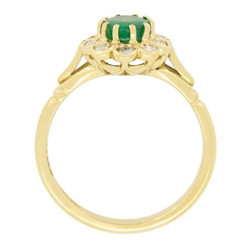 Ein 0,50 Karat schwerer Smaragd steht im Mittelpunkt dieses Vintage-Cluster-Rings. Der Smaragd ist ein oval geschliffener Stein, gefasst in 18 Karat Gelbgold. Um den zentralen Smaragd herum sitzt ein Cluster aus zehn runden Brillanten. Die Diamanten