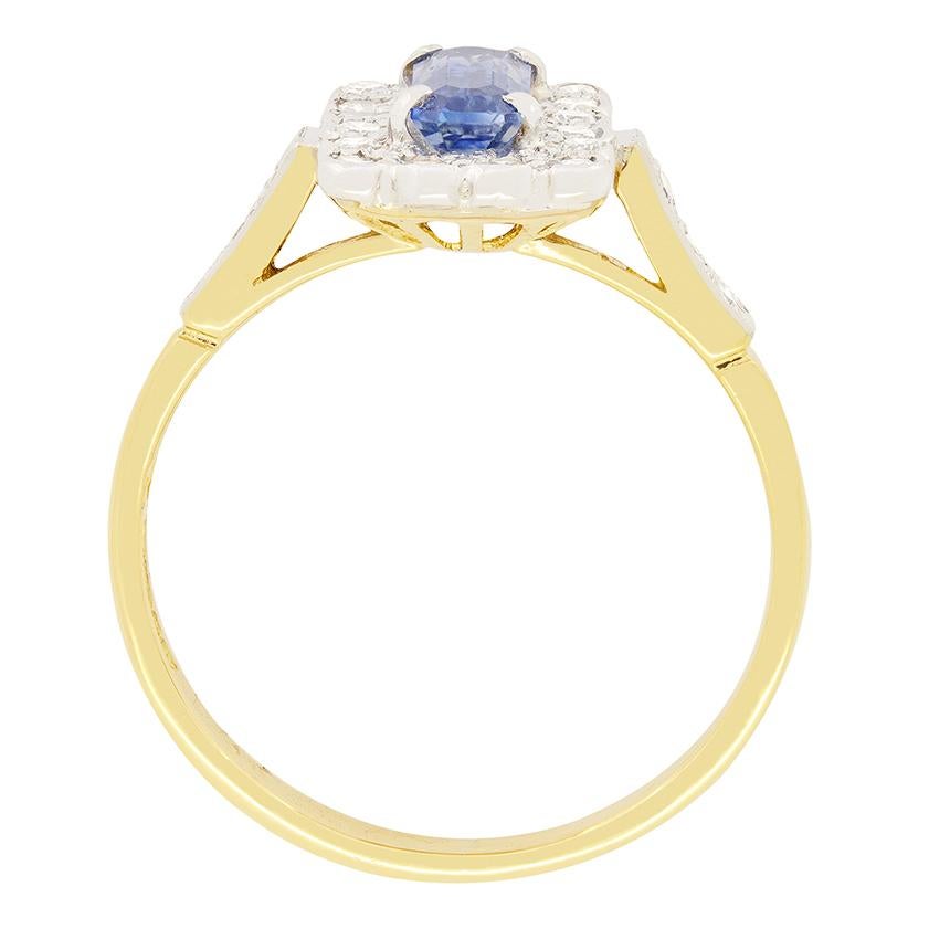 This elegant vintage cluster ring dates back to 1964.  The ring centres around a stunning light blue sapphire weighing 0.50 carat. The emerald cut sapphire is claw set in platinum and surrounded by 0.44 carat total of round brilliant diamonds, each