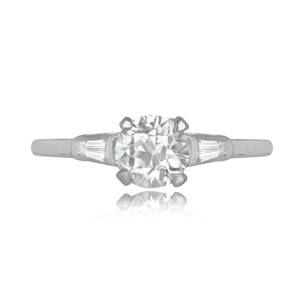 An exquisite vintage engagement ring showcases a prong-set old European cut diamond weighing around 0.57 carats, with L color and VS1 clarity. Its shoulders feature two tapered baguette diamonds, each weighing approximately 0.05 carats. This ring is