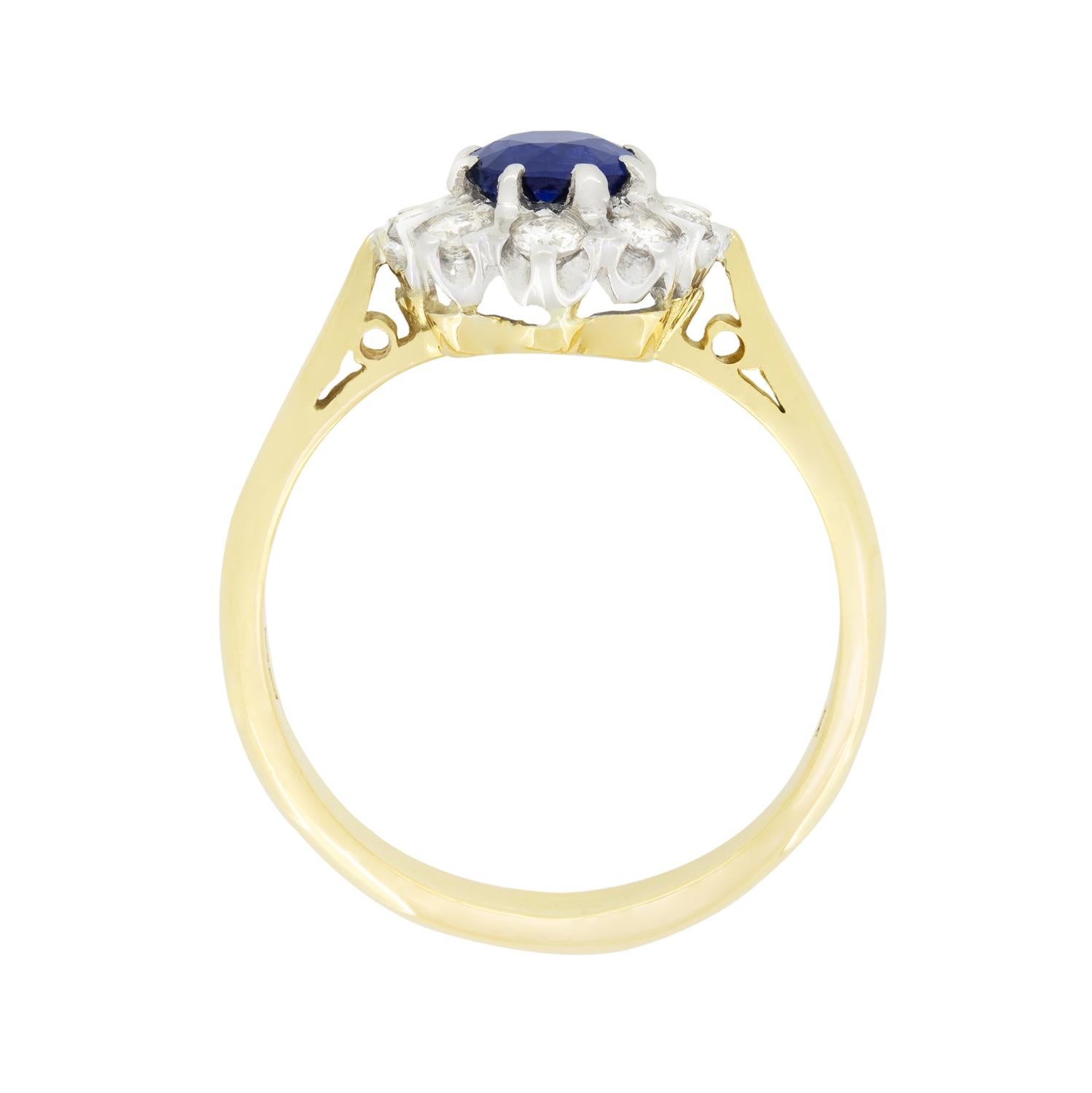 Cette magnifique bague vintage à grappes présente un saphir central entouré de diamants ronds de taille brillant. Le saphir de taille ronde est une pierre d'un bleu profond pesant 0,60 carat.  Les diamants entourés totalisent 0,40 carat, tous de