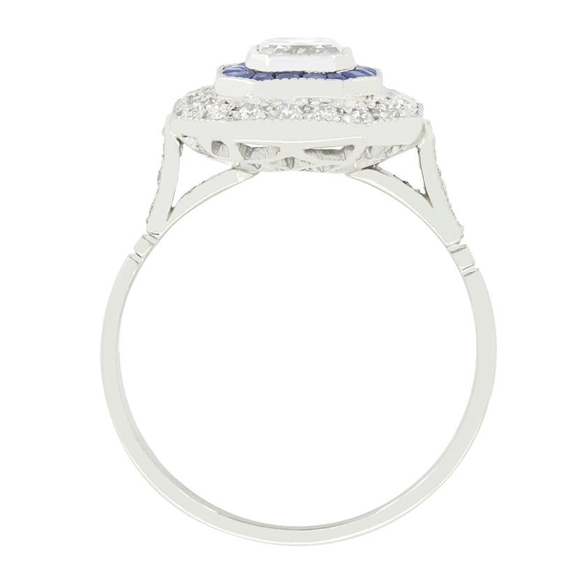 This beautiful vintage octagonal target ring dates back to the 1960s. It features an emerald diamond at its centre, weighing 0.70 carat. Graded highly at F in colour and VS2 in clarity, the diamond is rub over set to create a clean look. Surrounding