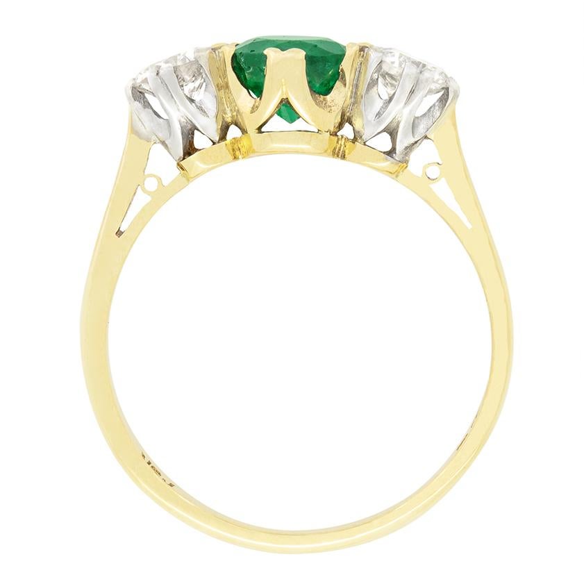 With hallmarks dating to 1986, this wonderful trilogy ring features a central emerald flanked by round brilliant diamonds. The characterful emerald is a round cut stone weighing 0.80 carat. The diamonds set to either side weigh 0.30 carat each and