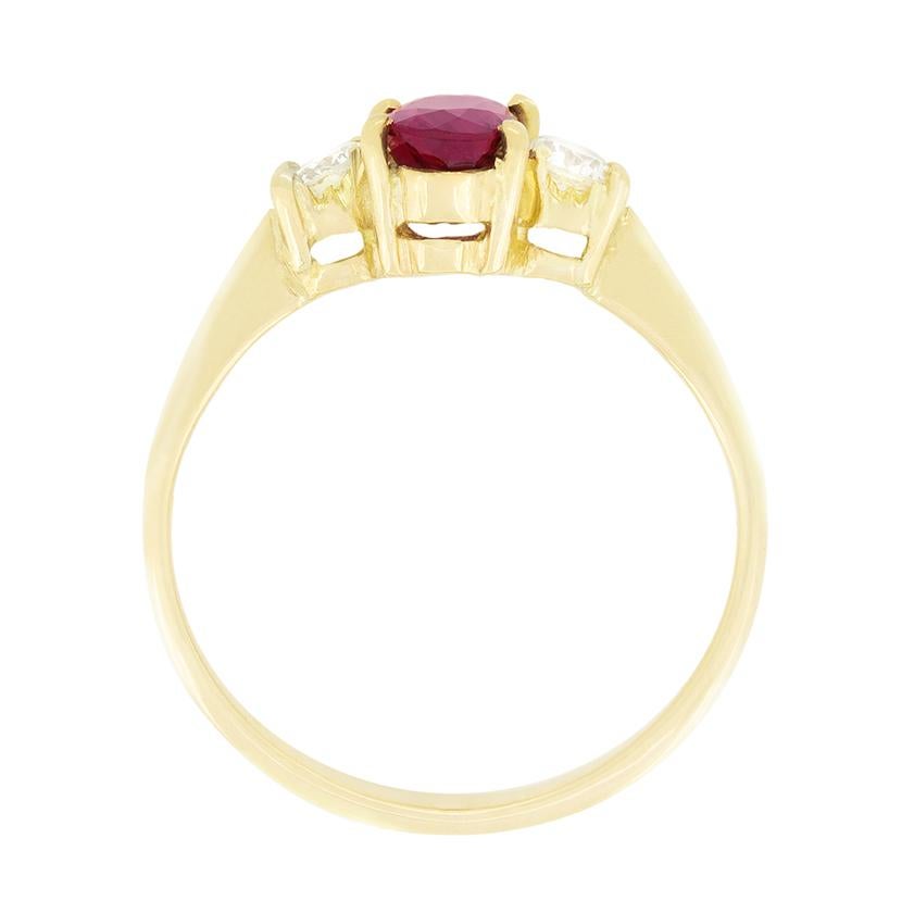 Un rubino ovale è affiancato da diamanti tondi e brillanti in questo anello a tre pietre degli anni Settanta. Il rubino è una pietra di 0,85 carati, mentre i diamanti che lo accompagnano sono di 0,10 carati ciascuno. I diamanti sono di alta qualità