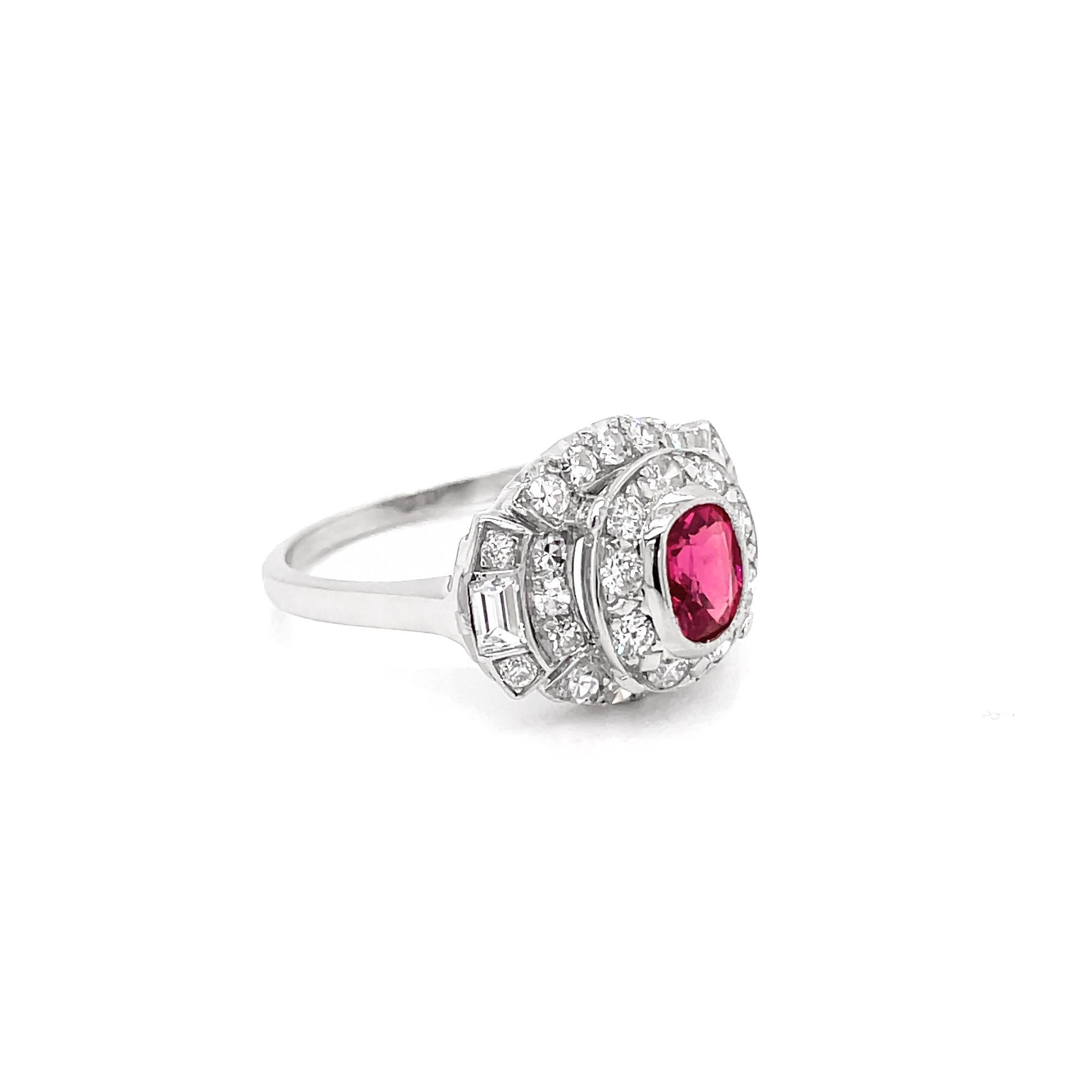 This gorgeous Deco style cluster ring features an oval pink spinel, weighing 0.89ct, rub-over set in the center of a round brilliant cut diamond halo raised mount. The ring is further decorated with a mixture of grain set eight cut diamonds and