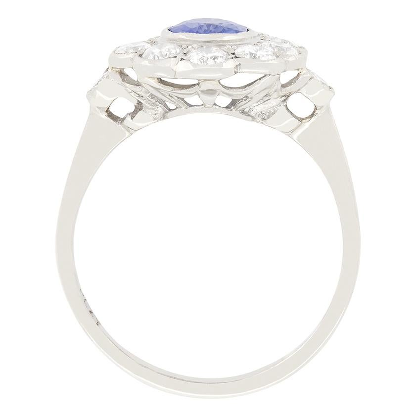 This beautiful cluster ring features a pale sapphire at its centre weighing 0.90 carat. The stone is rub over set into platinum, and surrounded by a halo of glistening round brilliant diamonds. The ten stones within the halo total 1.50 carat, with
