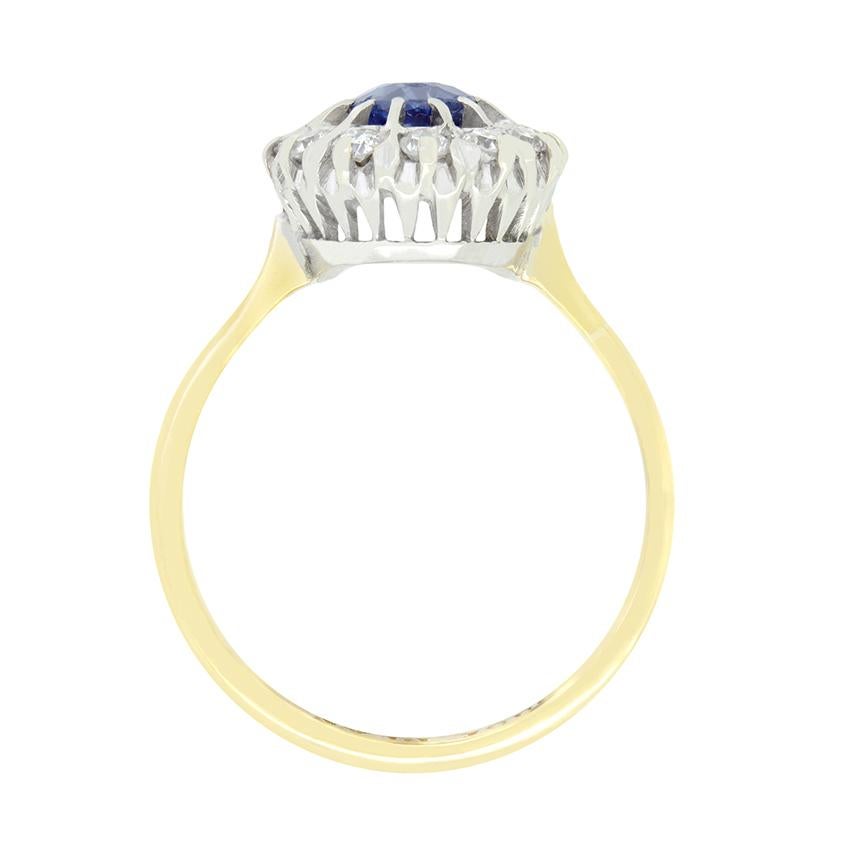 Ein auffälliges Naturprodukt steht im Mittelpunkt dieses Cluster-Rings im Vintage-Stil der 1950er Jahre. Der tiefblaue Saphir ist ein oval geschliffener Stein mit einem Gewicht von 0,90 Karat. Der zentrale Edelstein ist in einer erhöhten