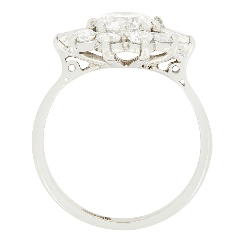 Este maravilloso anillo en racimo data de la década de 1950. En su centro se encuentra un brillante diamante redondo de 0,95 quilates. Este diamante central está rodeado por un grupo de diamantes brillantes redondos y una piedra de talla baguette en