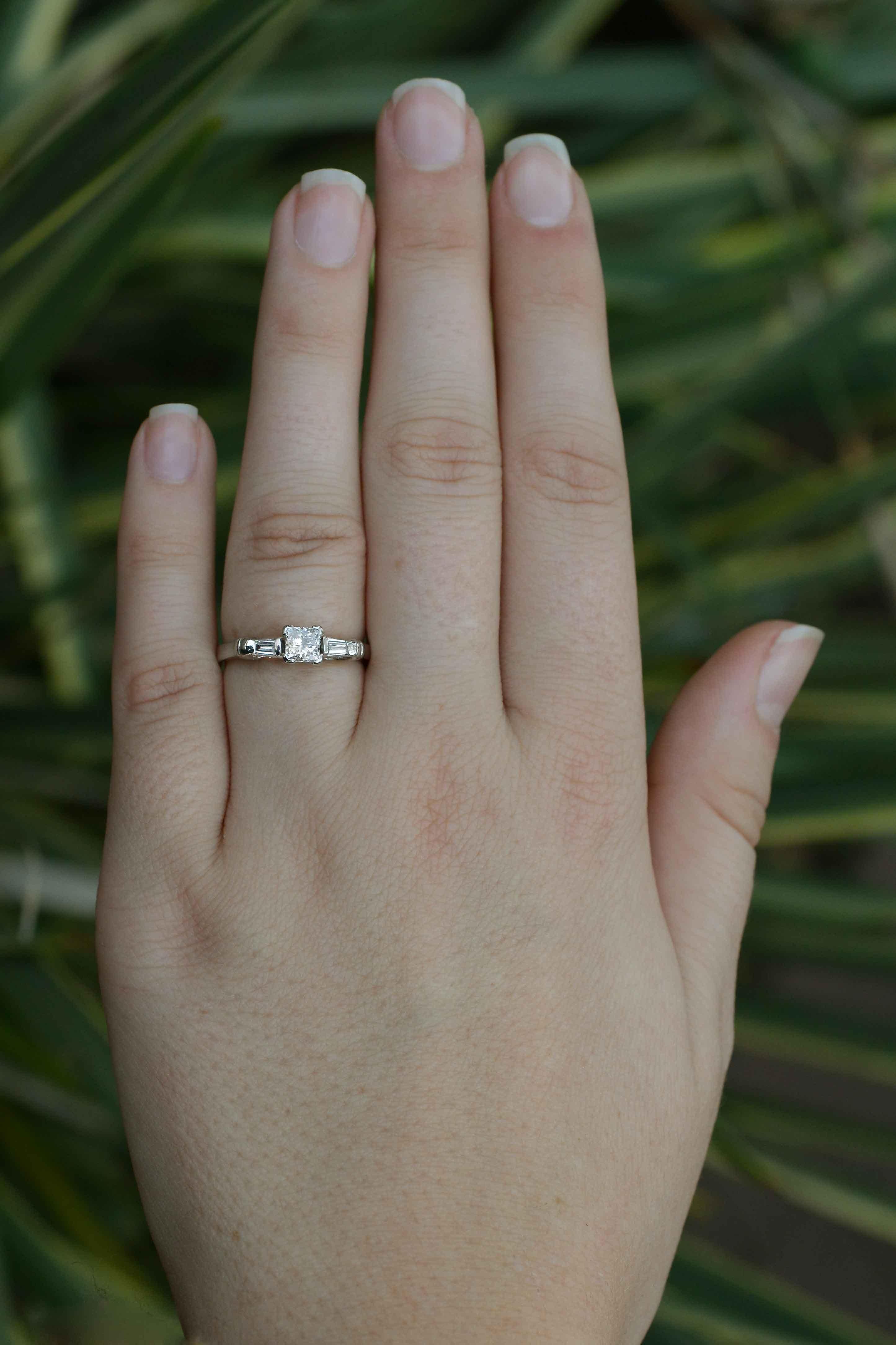 A dainty, vintage princess cut engagement ring. Focusing in on a near colorless diamond with linear, symmetrical facets that give it an incredible glisten. The low setting allows for an everyday wear and the 3 stone design is a classic that will you