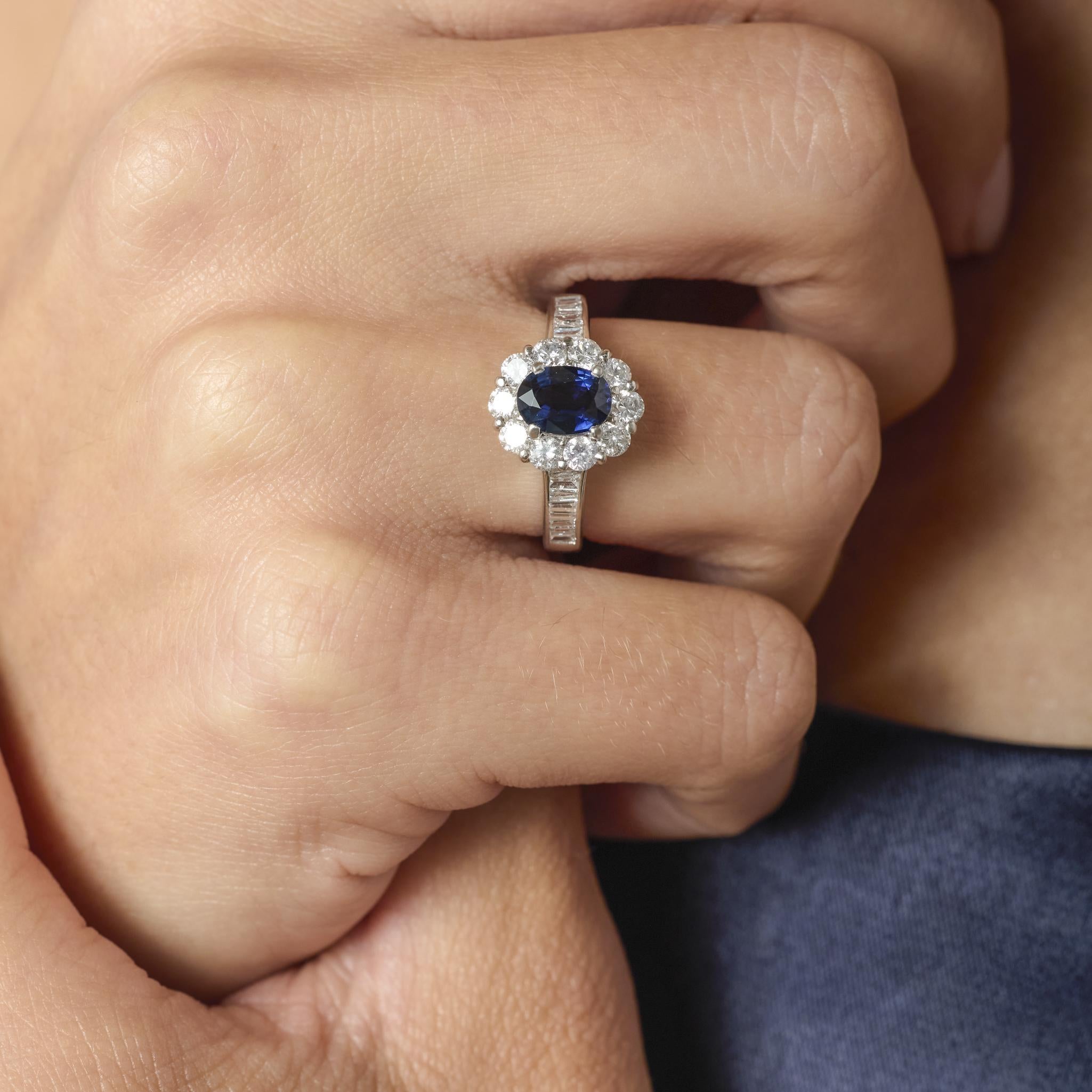 Dieser elegante und zeitlose Vintage-Cluster-Ring präsentiert einen ovalen blauen Saphir von 1,00 Karat, der in einer tiefen, bezaubernden Farbe strahlt. Der Saphir ist von einem funkelnden Halo aus sechsundzwanzig Diamanten umgeben - sowohl runde