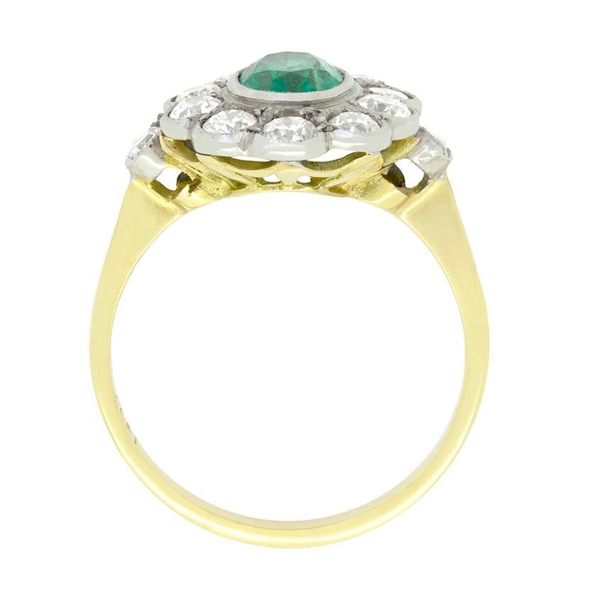Dieser bezaubernde Vintage-Cluster-Ring stammt aus den 1970er Jahren. In seinem Zentrum sitzt ein 1,00 Karat schwerer Smaragd, der oval geschliffen und in Platin gefasst ist. Um den zentralen Stein herum sind 1,00 Karat funkelnde Diamanten im