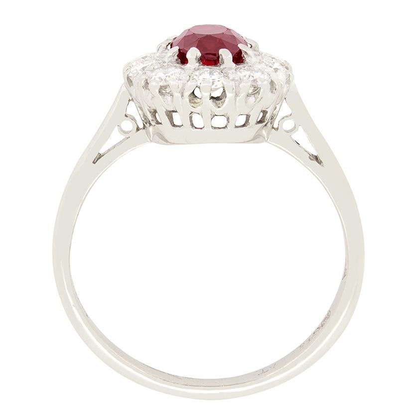 Un vibrante rubí rojo está envuelto por brillantes diamantes redondos en este anillo en racimo de los años 50. El rubí es una piedra de talla ovalada de 1,00 quilate. Engarzada en oro blanco de 18 quilates, la gema central resalta sobre la blancura