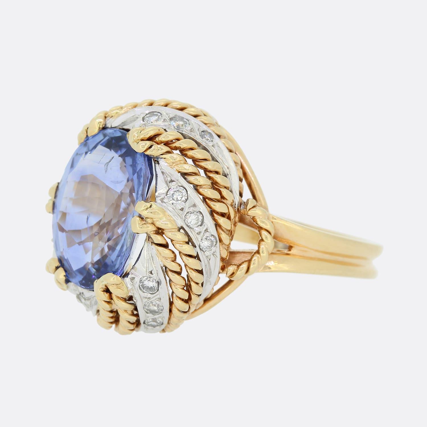 This is a vintage 18ct yellow gold, sapphire and diamond cocktail ring. The central sapphire is of Sri Lankan origin, heated and sits in six double claw mount. The ring mount has been crafted in 18ct yellow and white gold in an abstract rope style