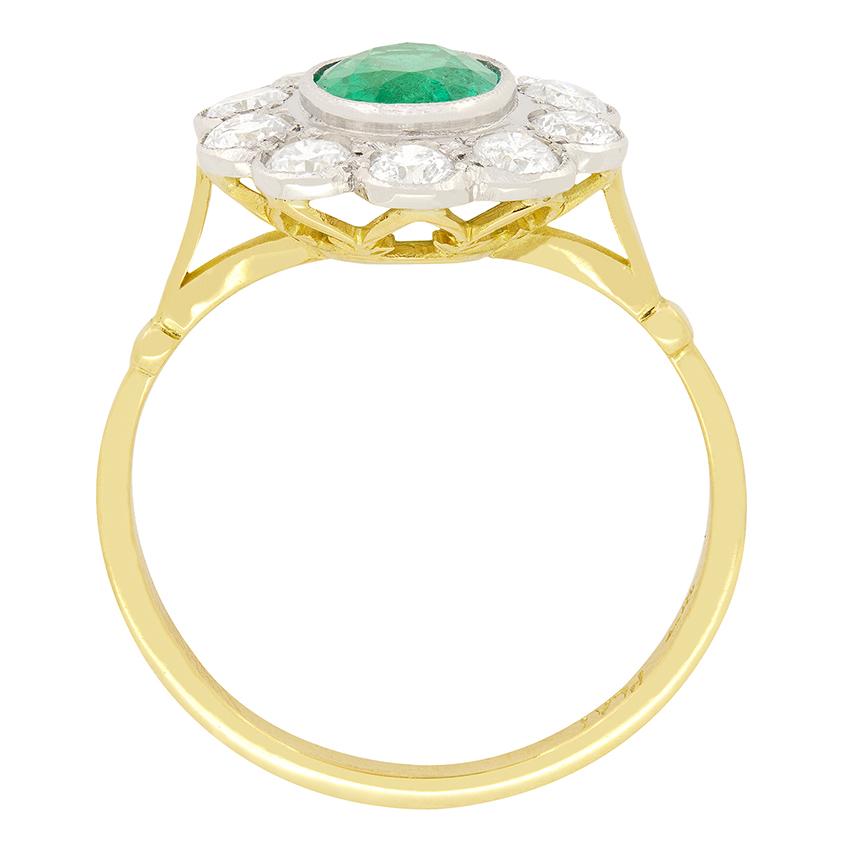 Dating to the 1950s, this beautiful cluster ring features a radiant green emerald in the centre. The emerald is an oval cut stone weighing 1.05 carat and is rub over set into milgrained platinum. Surrounding the emerald is a halo of sparkling white