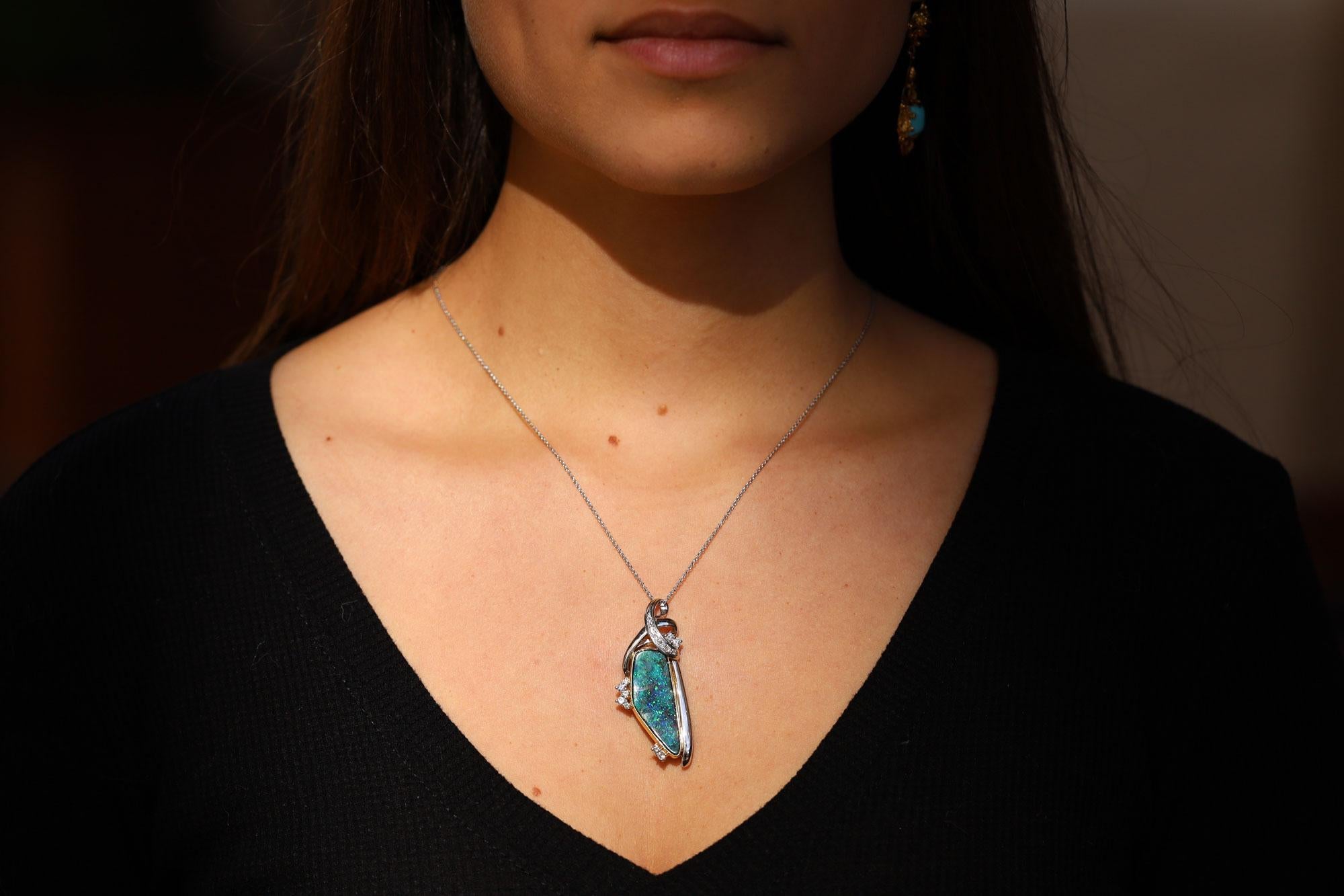 A fabulous vintage heirloom, this vivacious boulder opal pendant necklace is a statement of natural beauty. This impressive 10.74 carat gemstone is carved in a freeform, following the contours of the rough gem and showcased in yellow gold, platinum