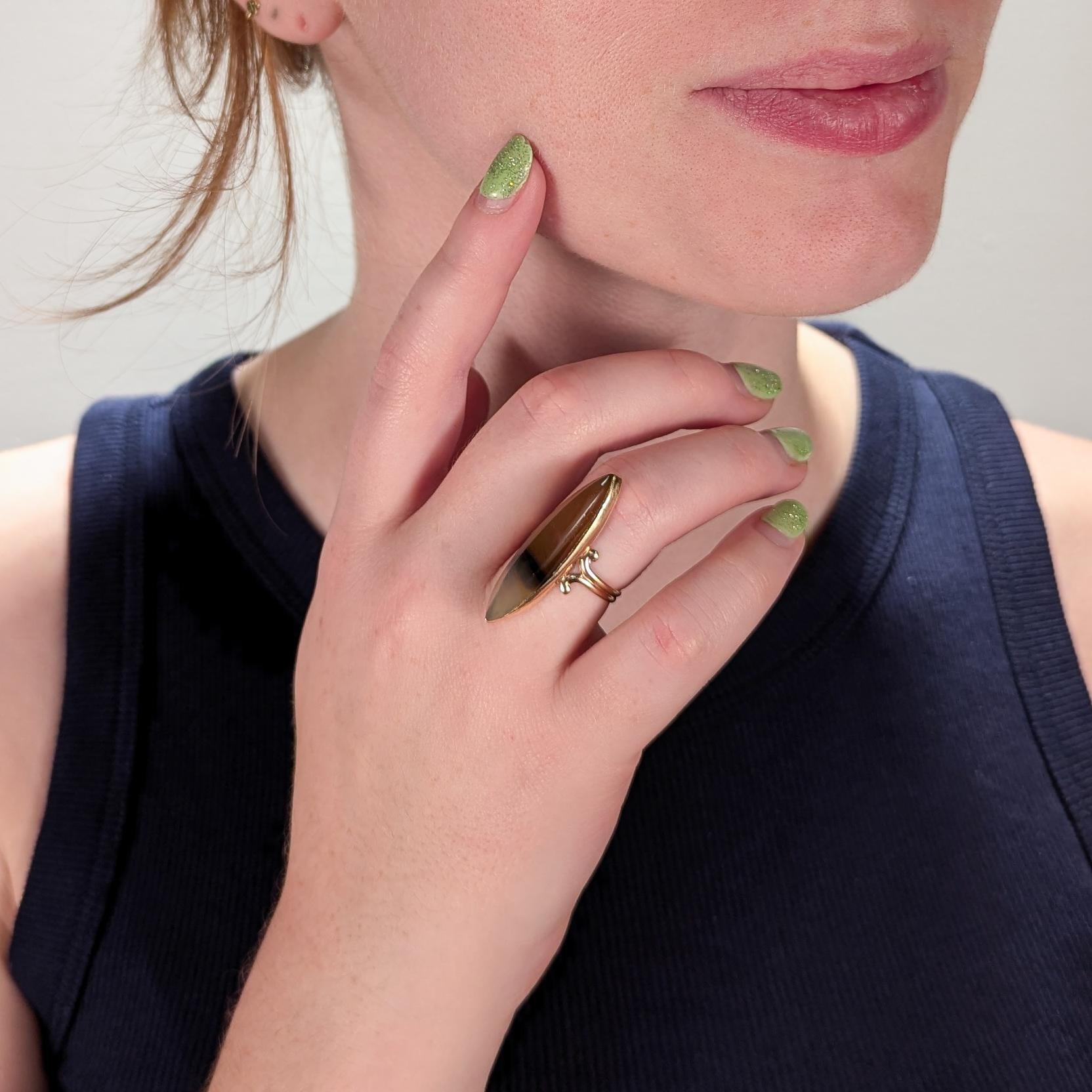 A fine navette shaped ring.

In 10 karat yellow gold.

Bezel-set with a long thin orange, brown, and cream colored agate navette cabochon.

Supported by a ram's horn split shank.

Marked 10k to the shank.

Simply a wonderful vintage