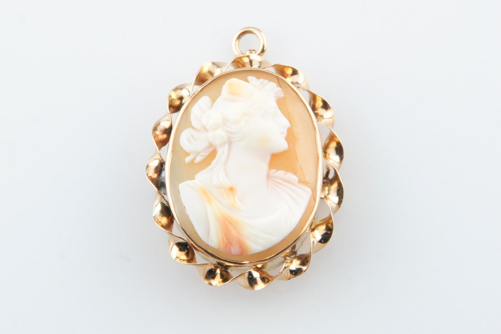 Bright Finish
Features a Carved Shell Cameo, Depicting the Dextral Formal Profile of a Woman
Measures 25 x 20 mm, 3.85 grams
Bezel Set Within a 10kt Yellow Gold Frame
Pin Shaft Holder and a Retracting Bail are On the Reverse Side of the