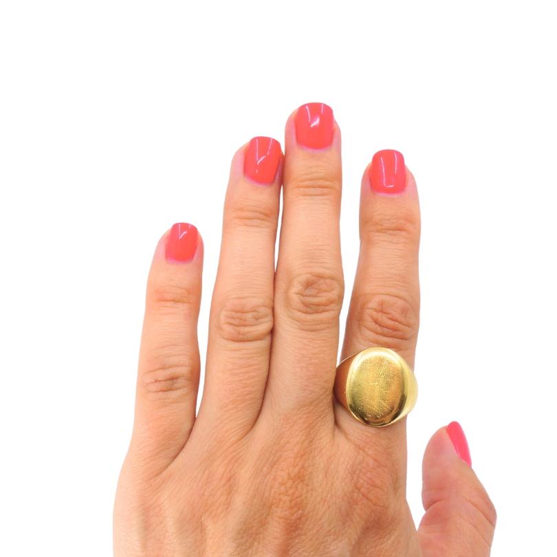 This classic vintage signet ring crafted in 10k yellow gold. Featuring a polished oval face engraved with an elegant monogram, this timeless ring offers both understated style and personal significance. The gleaming gold surface displays fine