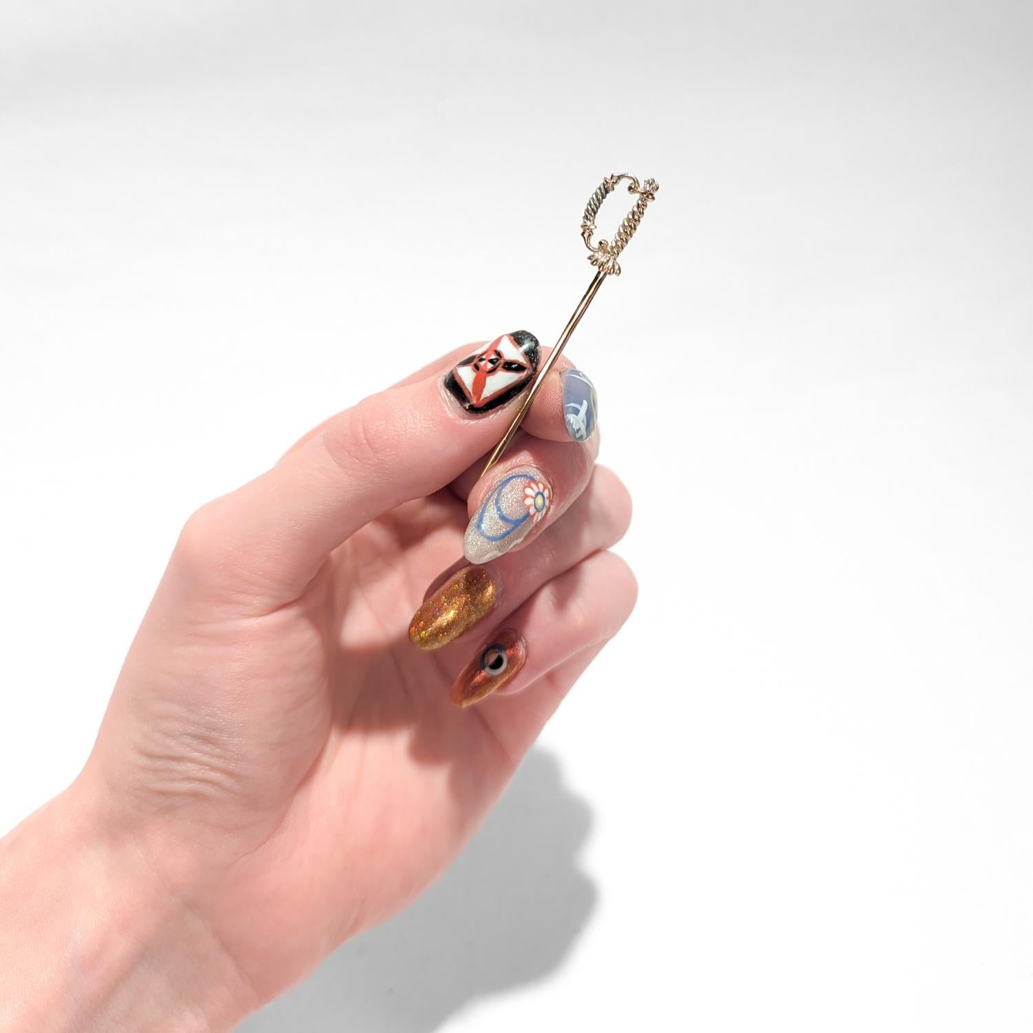 A fine vintage figural stickpin.

In the form of a small sword (épée de cour), the French thrusting sword from which the fencing's epee is derived.

With a prong-set round cut diamond to the pommel and silver accents to the guard.

Simply a