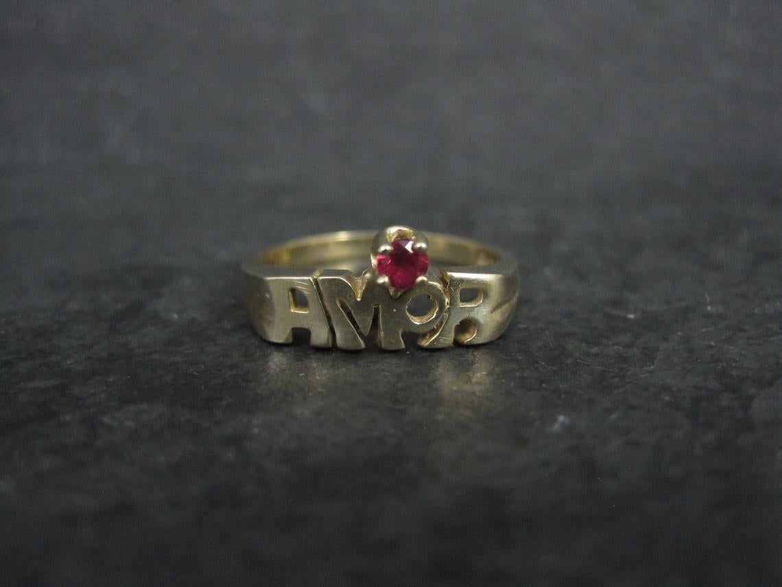 This beautiful vintage ring is 14k yellow gold.
It features the Spanish word for Love, AMOR and a stunning little 3mm pink ruby gemstone.

The face of this ring measures 5/16 of an inch north to south.
Size: 6 1/2
Marks: PC, 10K

Condition:
