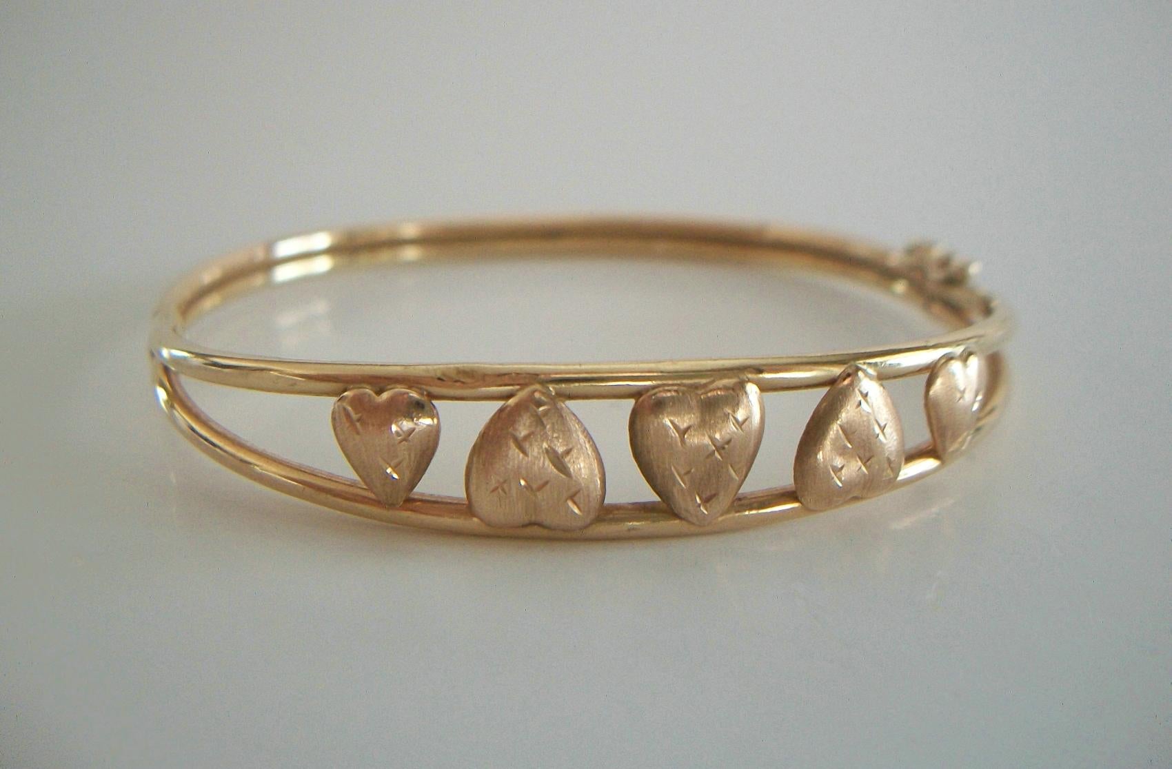A. A. J. - Vintage 10K yellow gold bangle bracelet with five applied hearts - each heart with stamped star detail - hinged assembly with tongue & groove clasp and double safety catch - signed on the back - U.S.A. - circa 1980's.

Excellent vintage