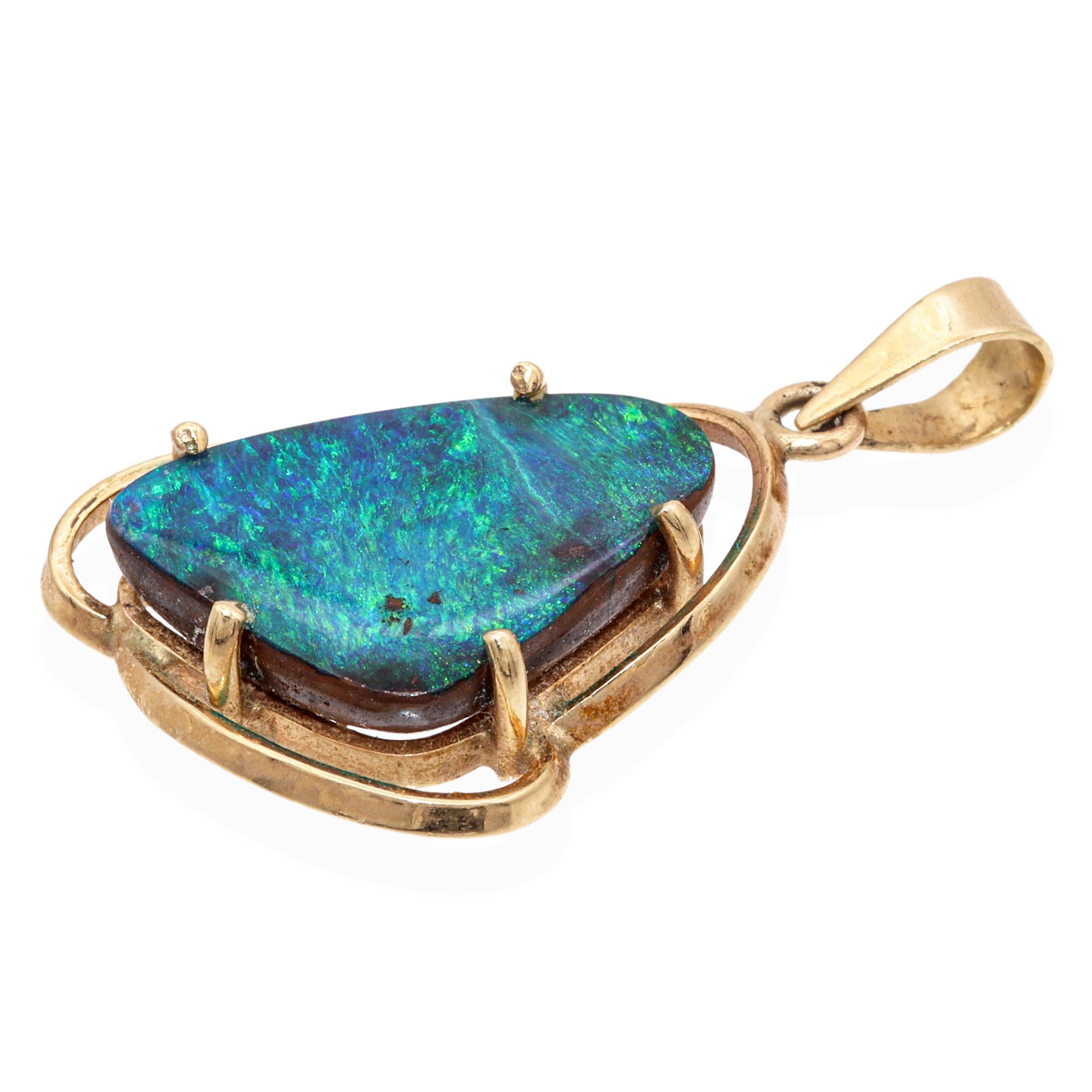 Ce pendentif vintage saisissant est réalisé en or jaune 10k et met en valeur une opale naturelle de forme libre avec des éclats captivants de bleu et de vert. L'opale est solidement sertie à l'intérieur d'une monture en or ouverte et fluide qui